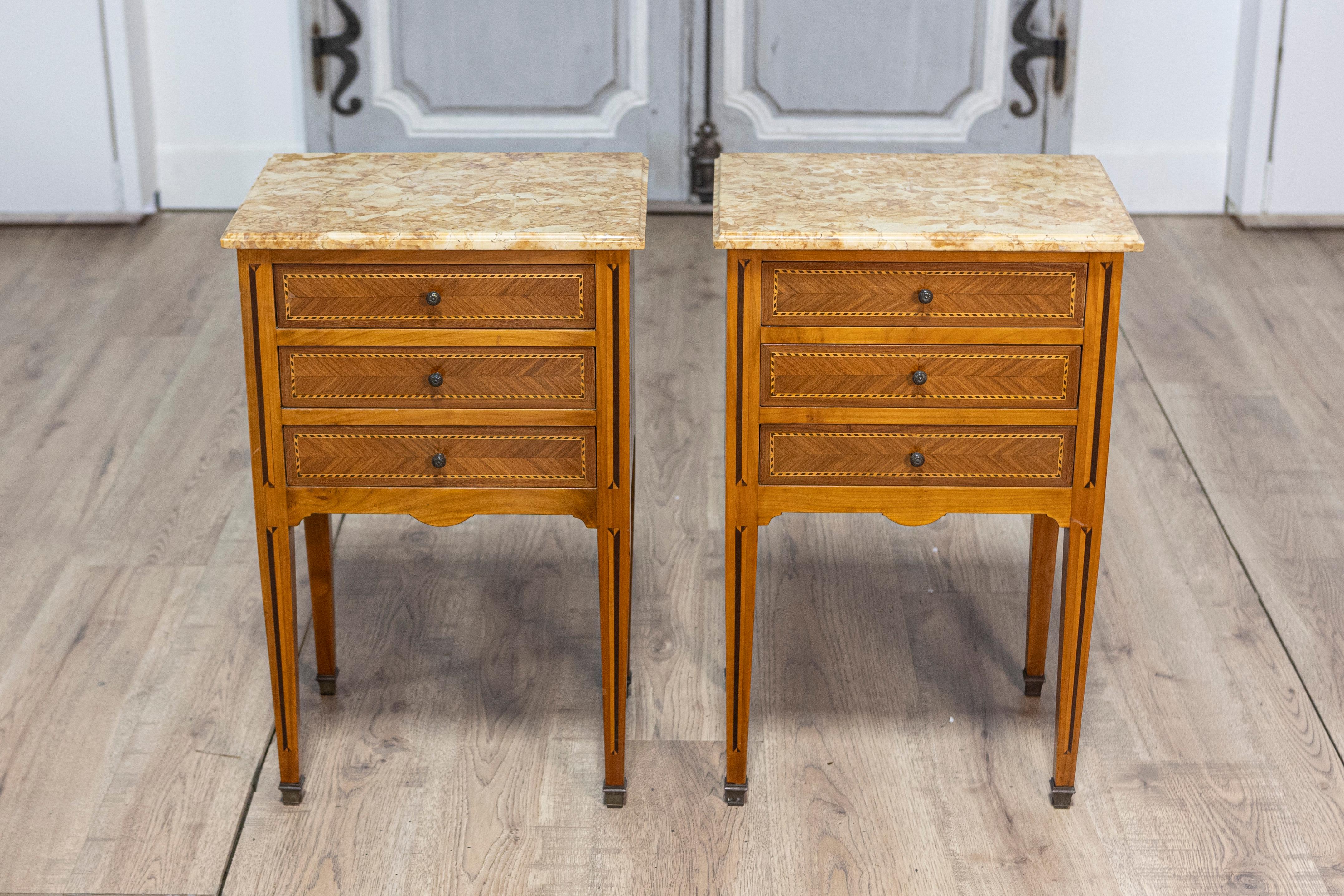 This elegant pair of early 20th-century French bedside tables combines refined craftsmanship and timeless design. Each table features a rectangular marble top with soft veining, providing a luxurious and durable surface. Below, three drawers adorned