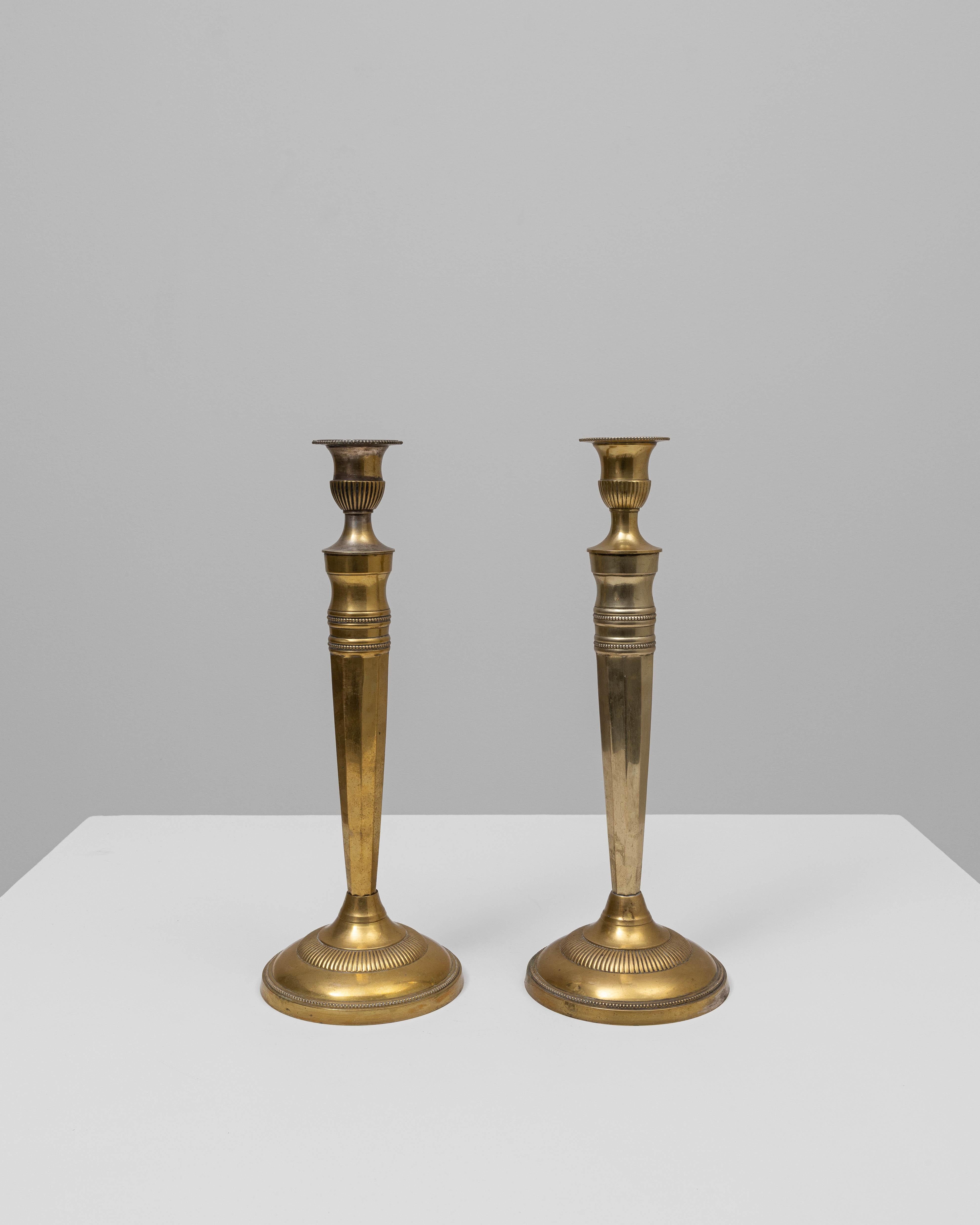 Questa coppia di candelieri in ottone francese del XX secolo presenta una raffinata Silhouette allungata che unisce l'ispirazione classica a una sobria eleganza. Ogni candeliere è realizzato con una colonna affusolata e sfaccettata che si innalza da