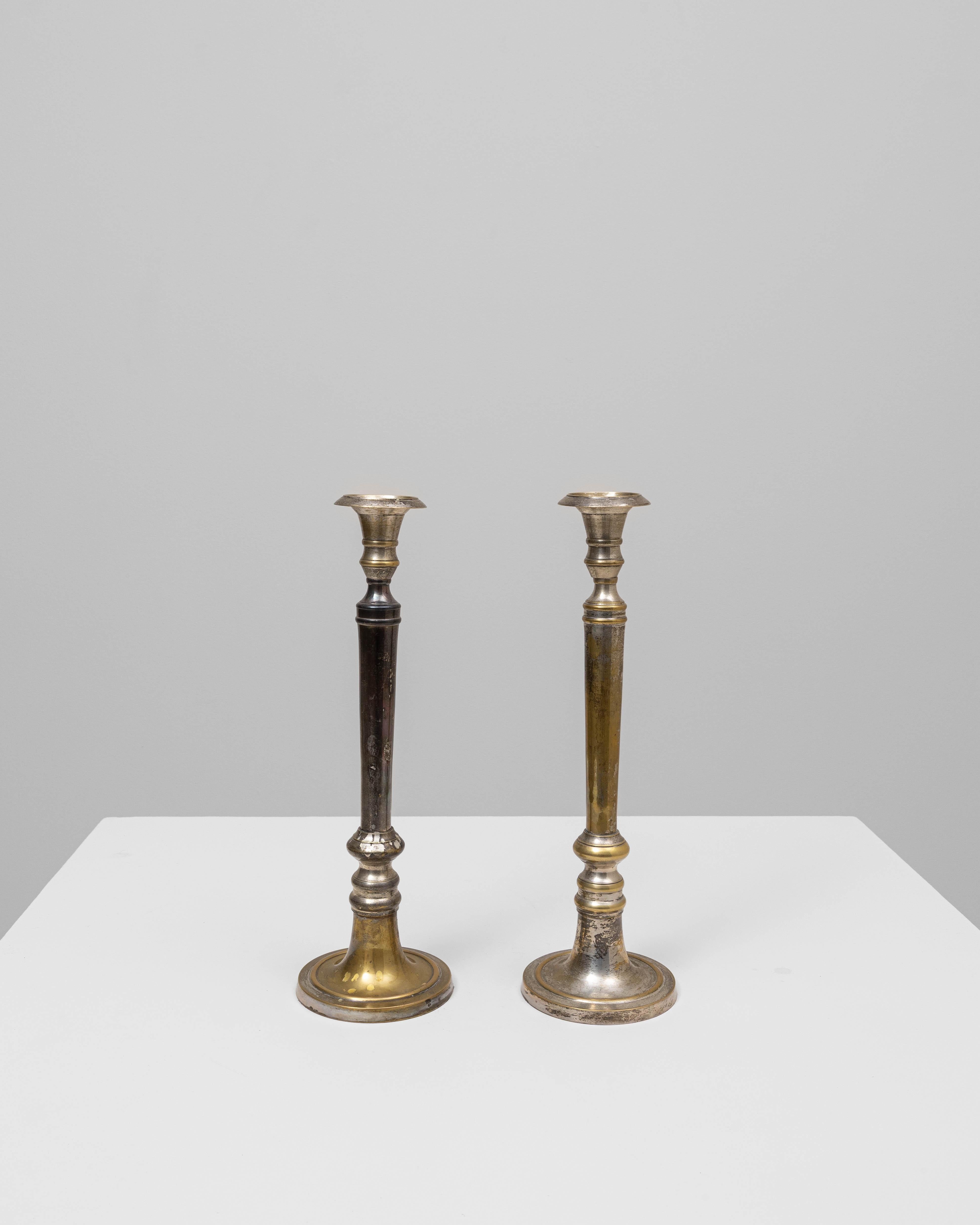 Questa coppia di candelieri in ottone francese del XX secolo mostra un carattere elegante e consumato da decenni di patina naturale. Ogni pezzo è caratterizzato da una colonna sottile e allungata, accentuata da una sottile tornitura e da dettagli