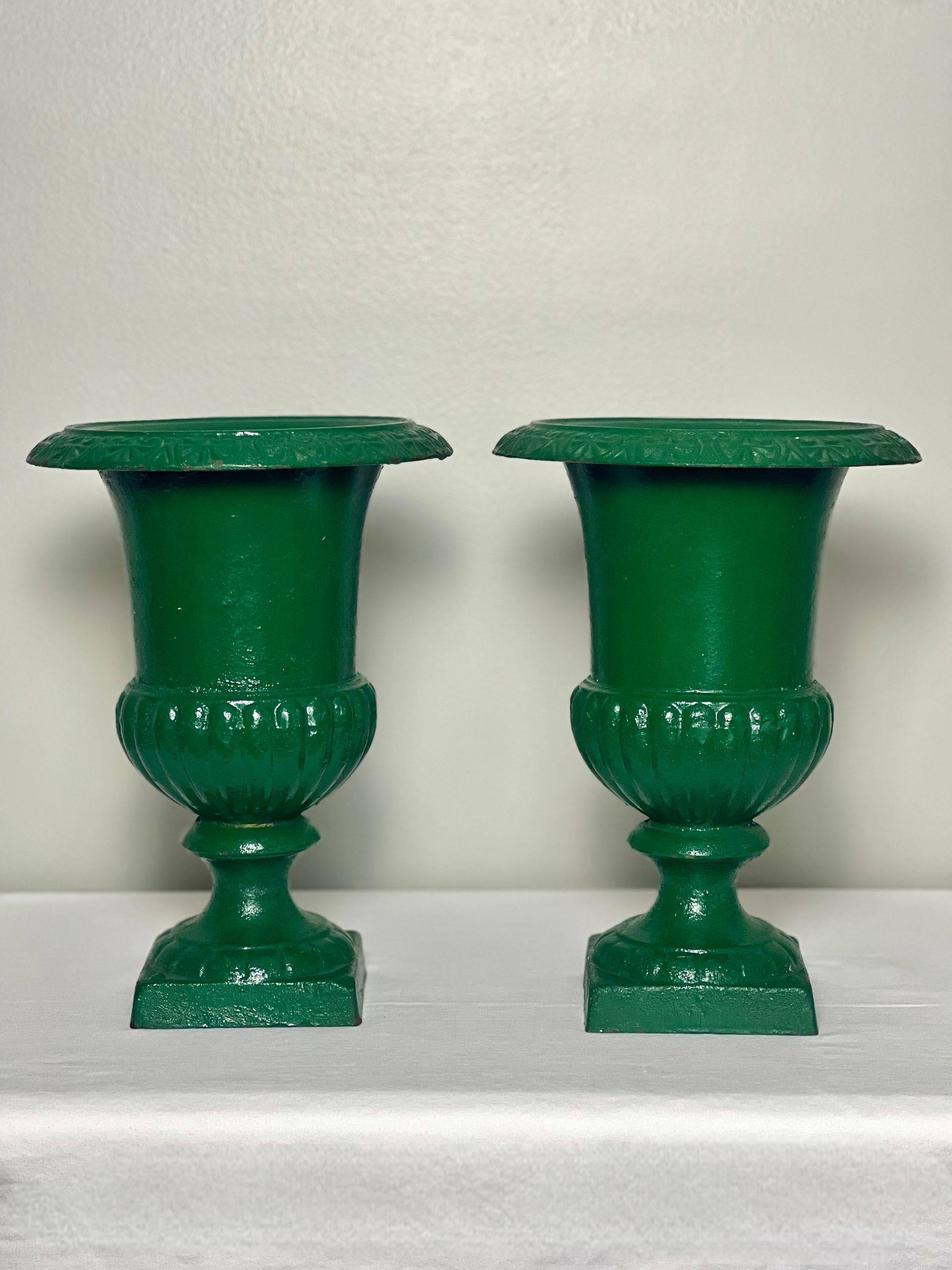 Beautiful pair of green painted French Medici style cast iron urns, early 20th century. Classic design with a gadrooned, bell-shaped body and decorated flared rim with a round foot on an integrated square plinth base. The lively green brings great