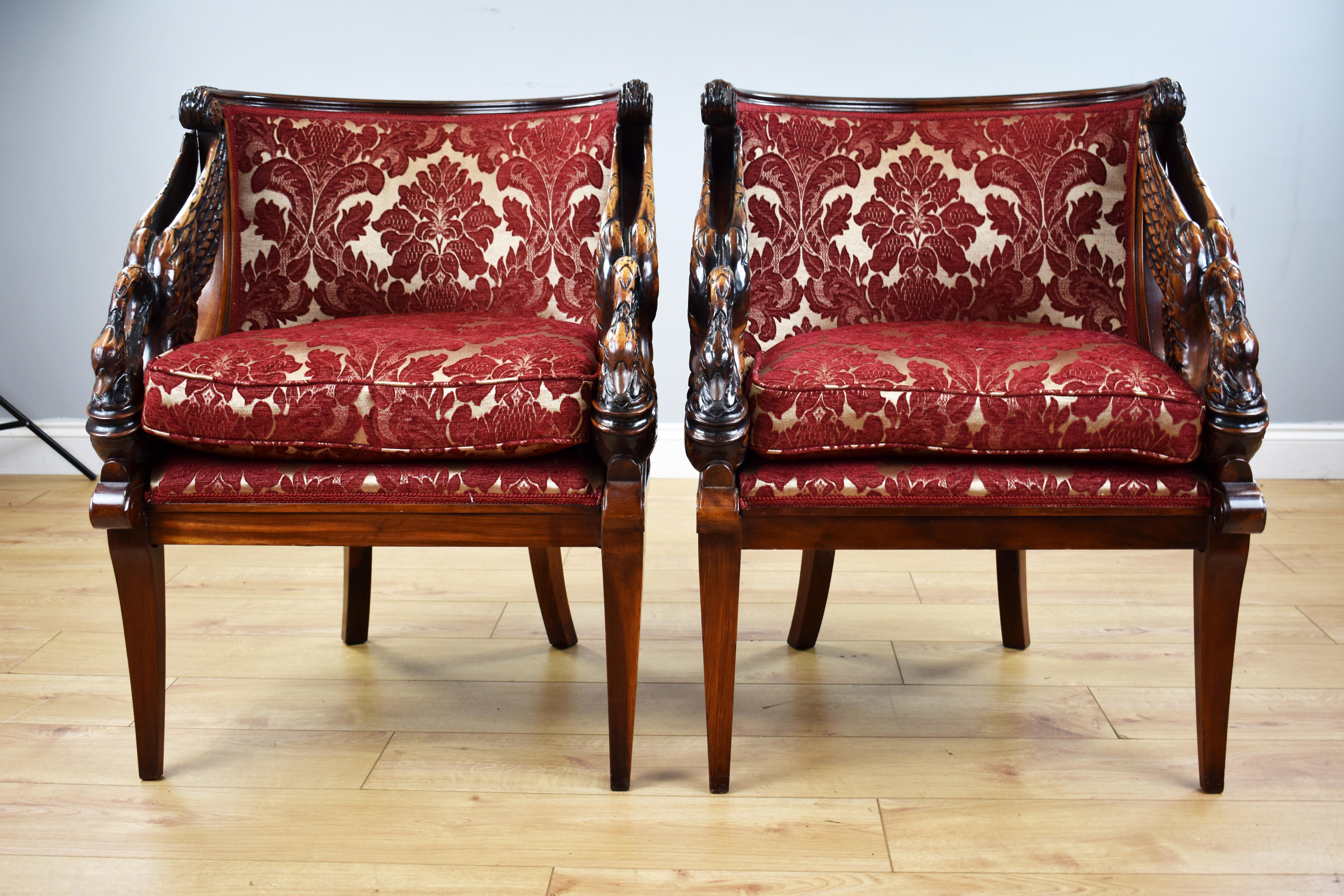 For sale is a pair of good quality French Empire style tub chairs, each with mahogany frames and ornately carved swan arms, standing on splayed legs. Each chair is upholstered in a red damask with a medallion pattern and both chairs are in very good