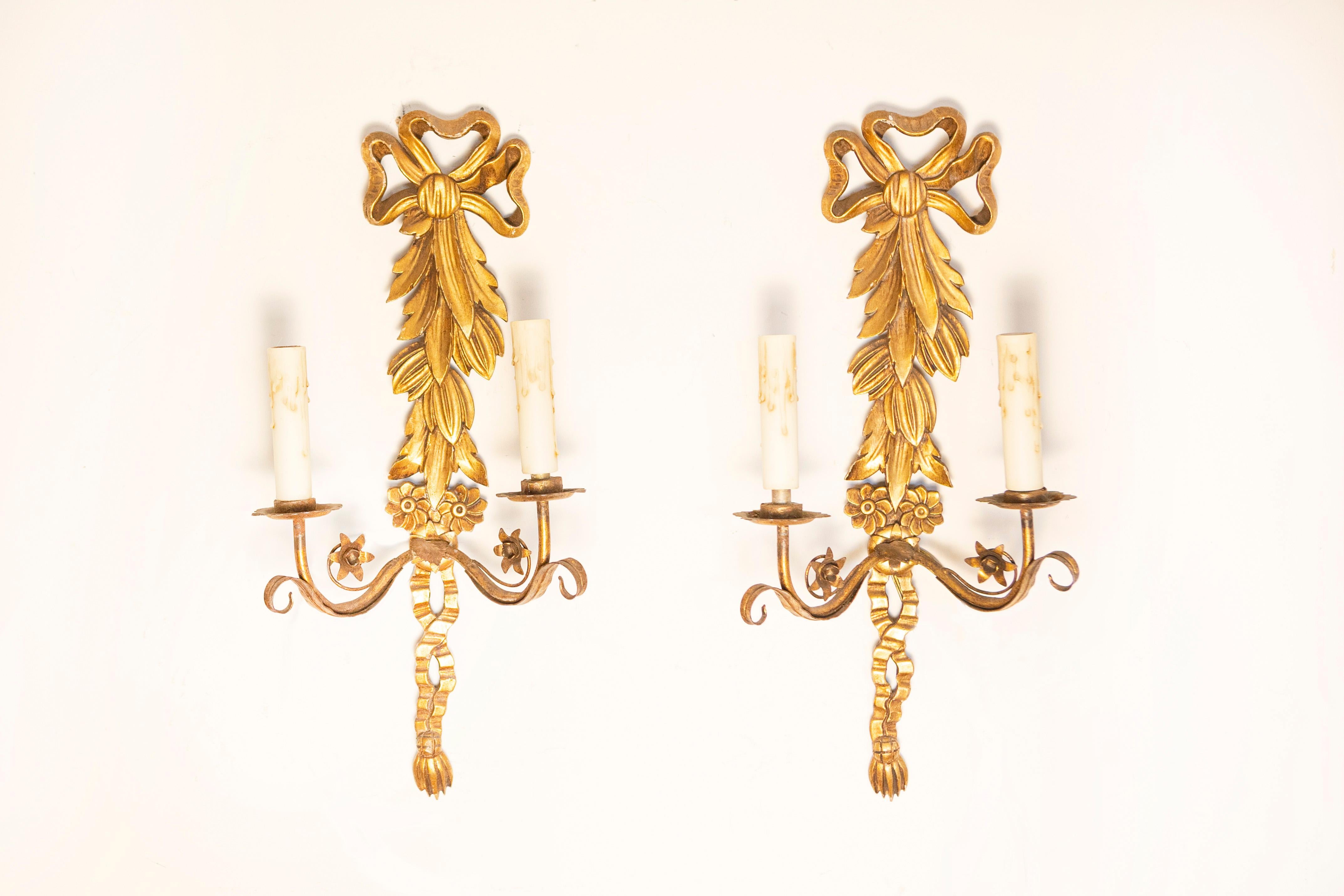 Cette étonnante paire d'appliques françaises en bois doré du XXe siècle est une parfaite incarnation de l'élégance intemporelle et de l'artisanat. Chaque applique présente un design magnifiquement sculpté, orné de détails complexes tels qu'un