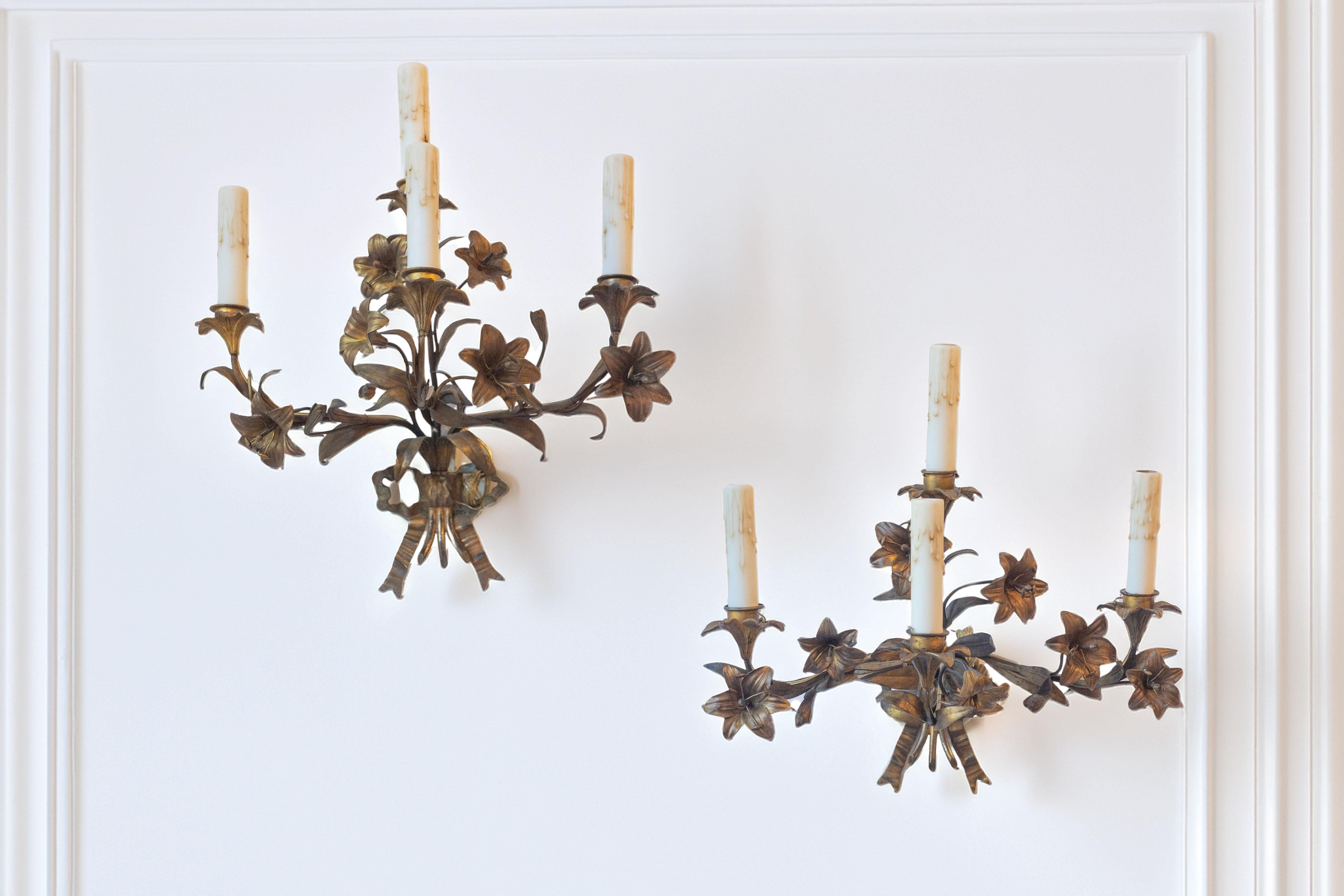 Un'affascinante coppia di applique francesi dorate del XX secolo, caratterizzate da un motivo floreale ben dettagliato. Ogni applique ha tre bracci ornati da gigli e fogliame in metallo finemente scolpiti, che emanano una graziosa eleganza organica.