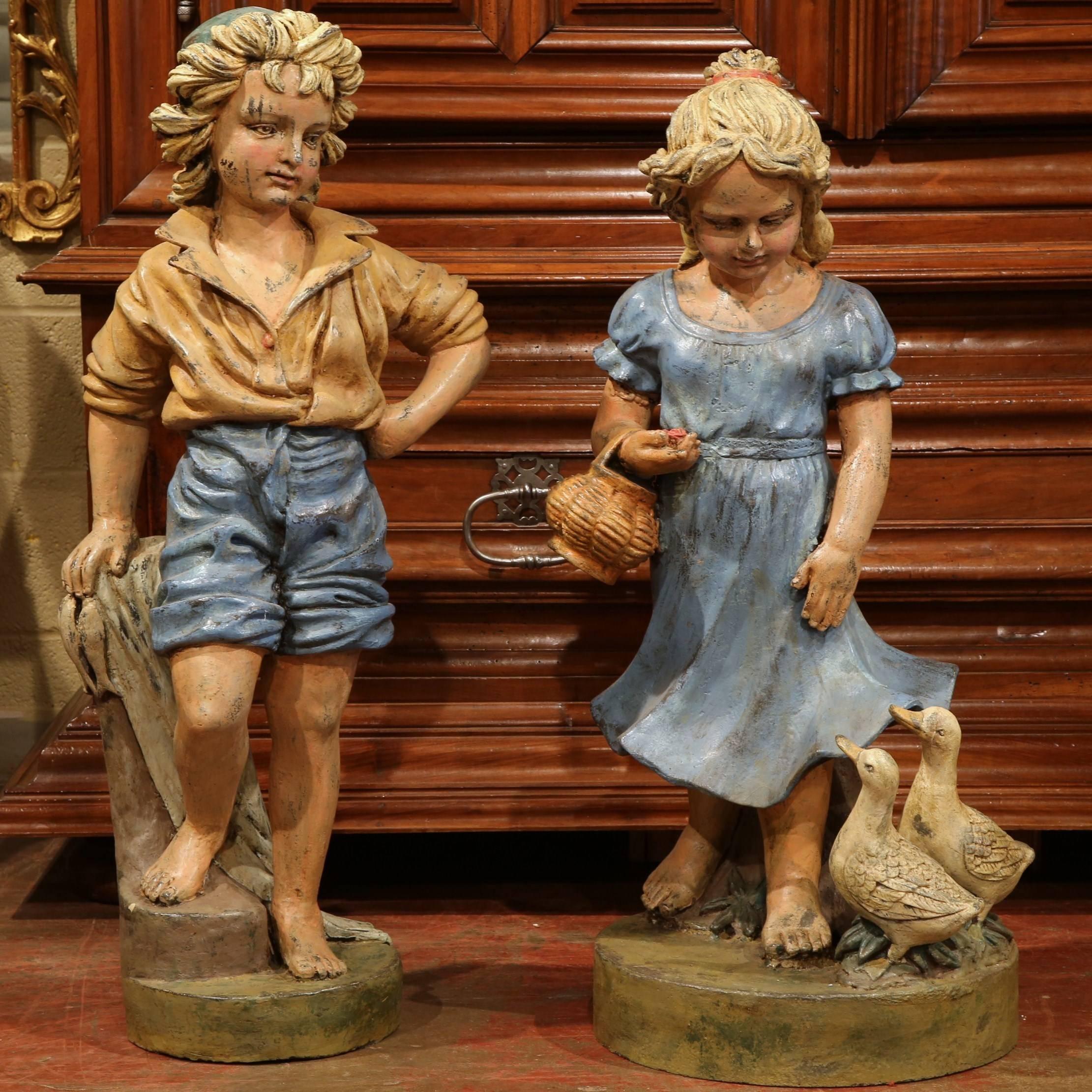 Add the charm of the French countryside to your home with this colorful pair of painted iron statues from Provence, France, circa 1970. The expressive figures depict a pair of children standing on round bases. The girl holds a basket with two ducks