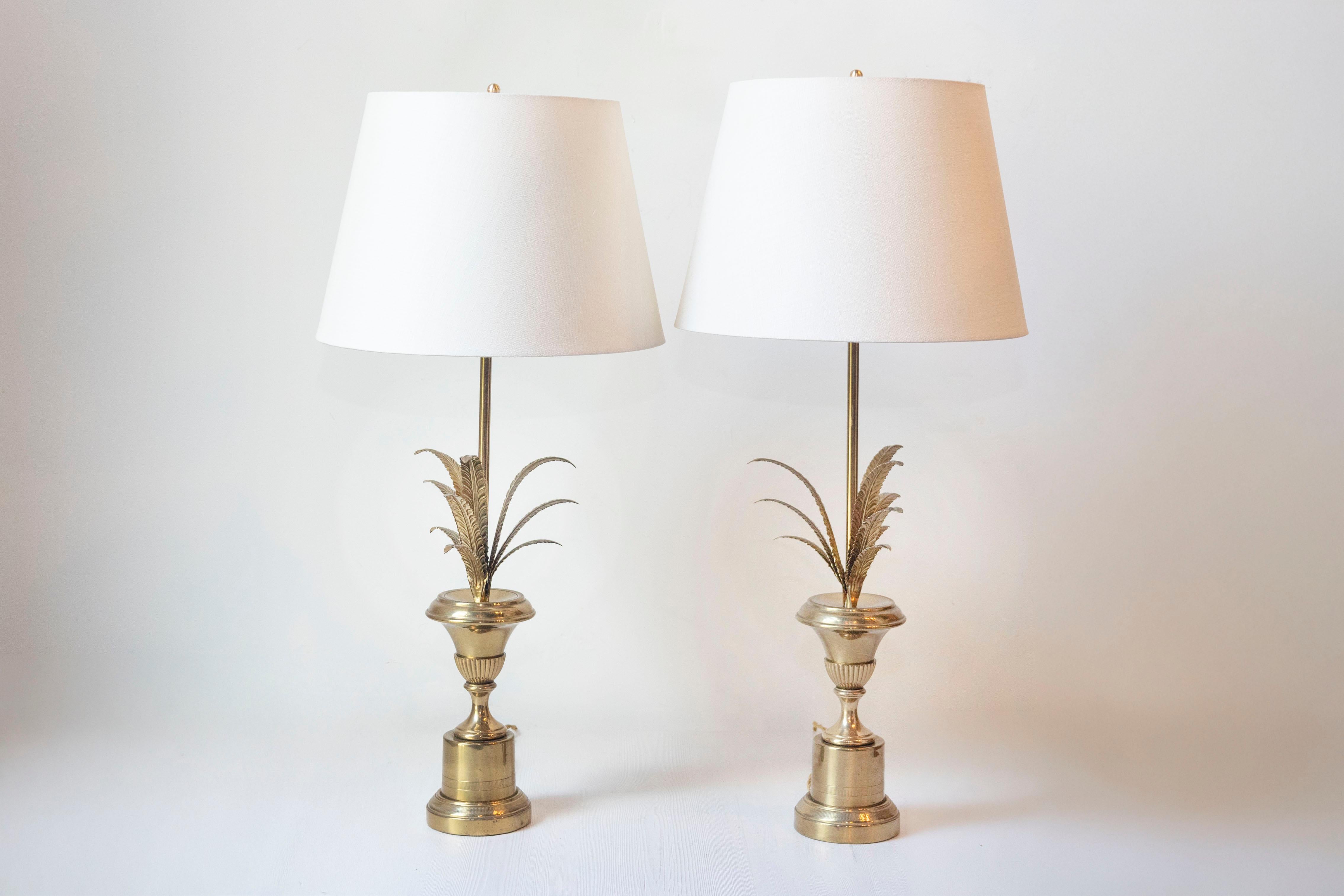 Cette élégante paire de lampes de table françaises du XXe siècle s'inspire du style renommé de la Maison Charles. Chaque lampe est ornée d'une feuille de palmier sculpturale s'élevant d'une base classique en forme d'urne, fabriquée en bronze doré