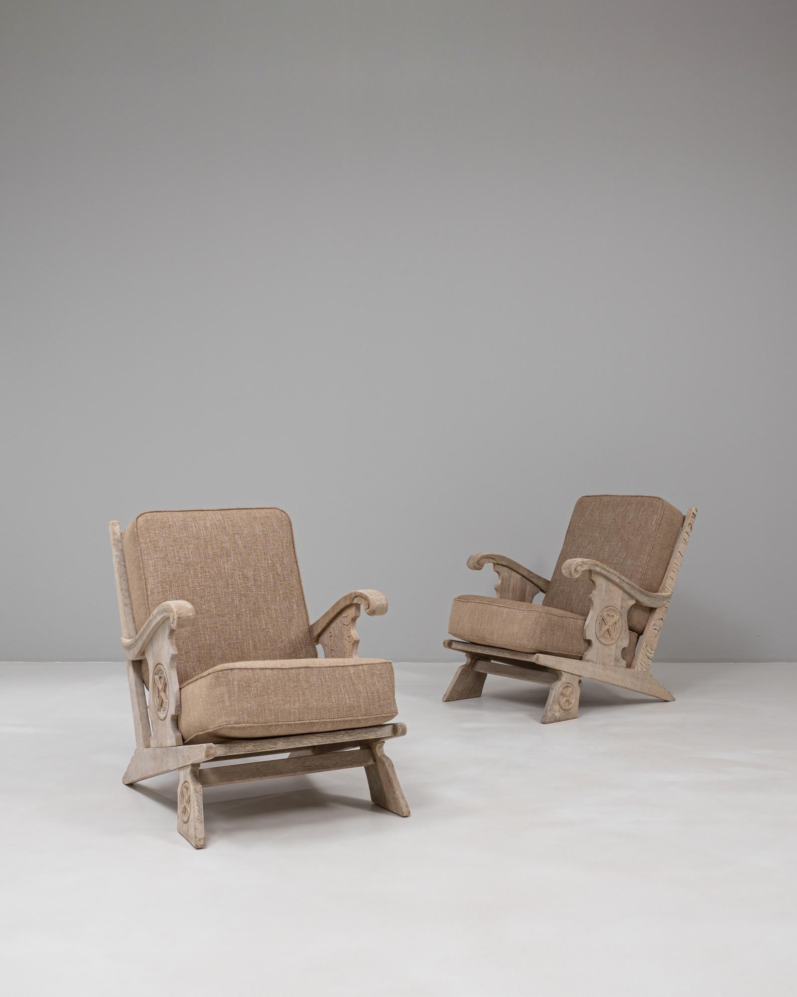 This pair of 20th Century French oak armchairs features a striking, carved silhouette that blends rustic craftsmanship with sculptural presence. Each chair is constructed from solid oak with a light, textured patina that highlights the natural grain