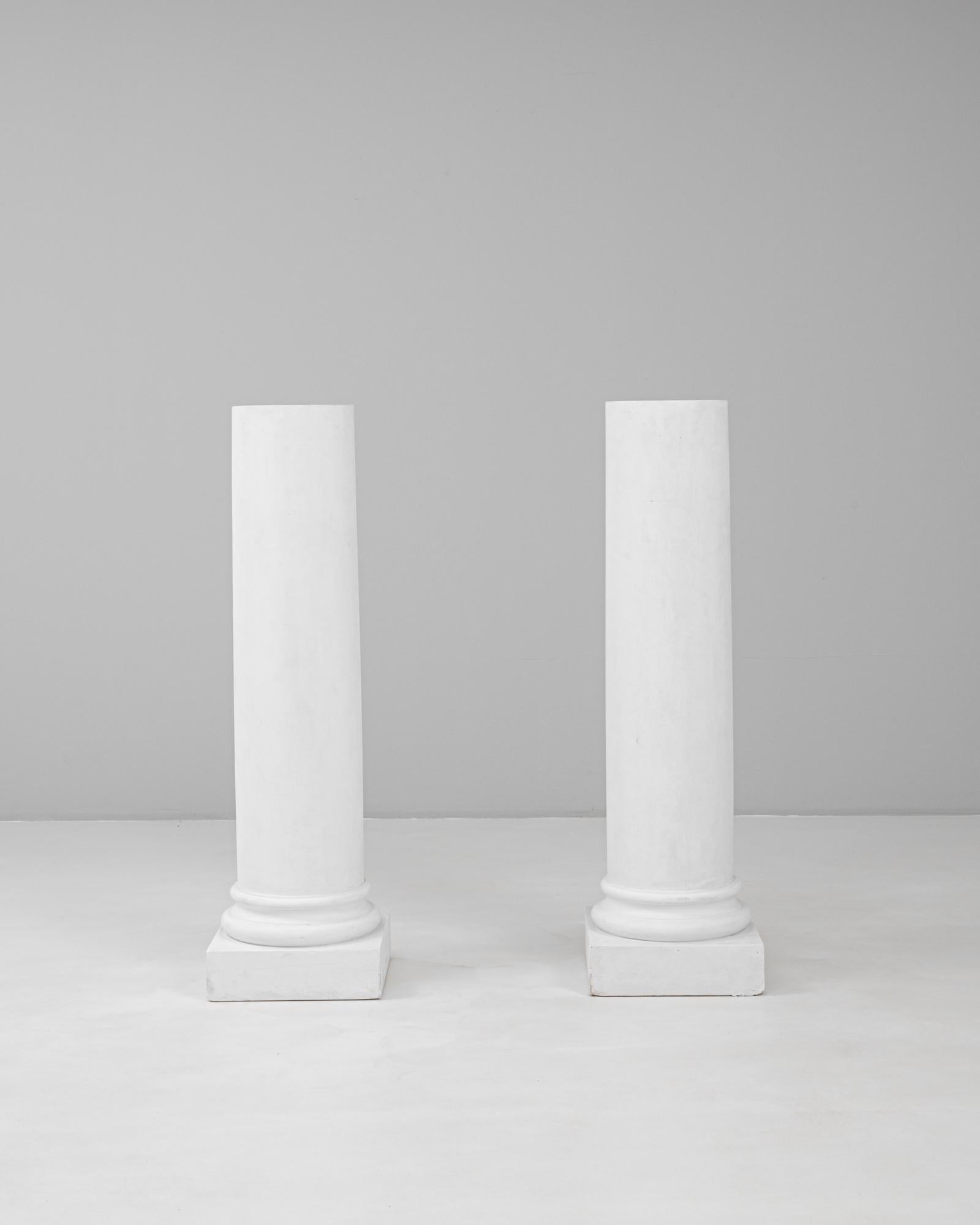 Questa coppia di colonne in gesso francese del XX secolo offre una presenza architettonica pulita con un'influenza classica senza tempo. Ogni colonna è caratterizzata da un fusto cilindrico liscio che poggia su uno zoccolo quadrato, con una semplice
