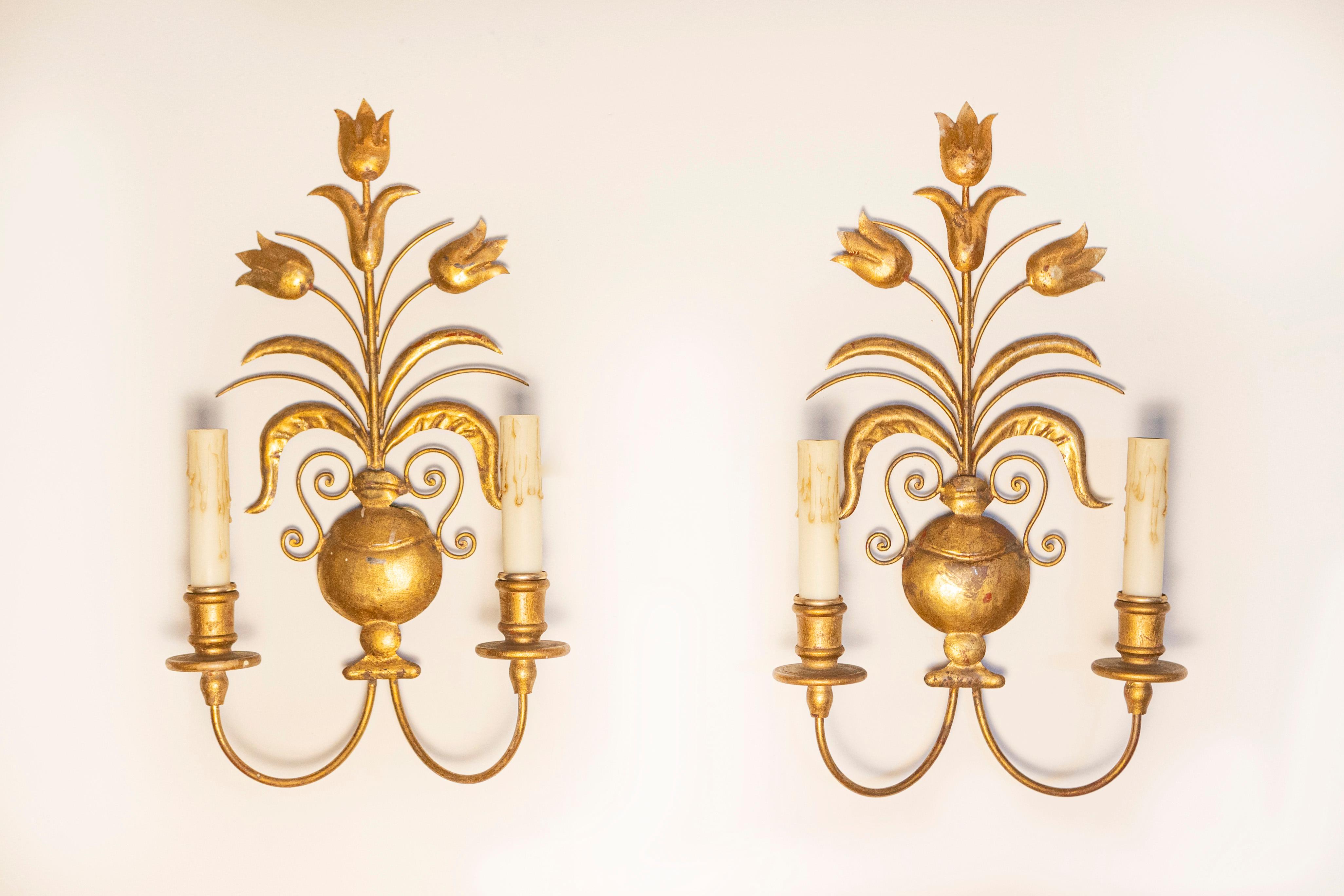 Cette étonnante paire d'appliques françaises du XXe siècle est un exemple d'élégance intemporelle et de design français classique. Fabriquées en métal doré, ces appliques sont ornées de motifs floraux complexes, avec des décorations en forme de