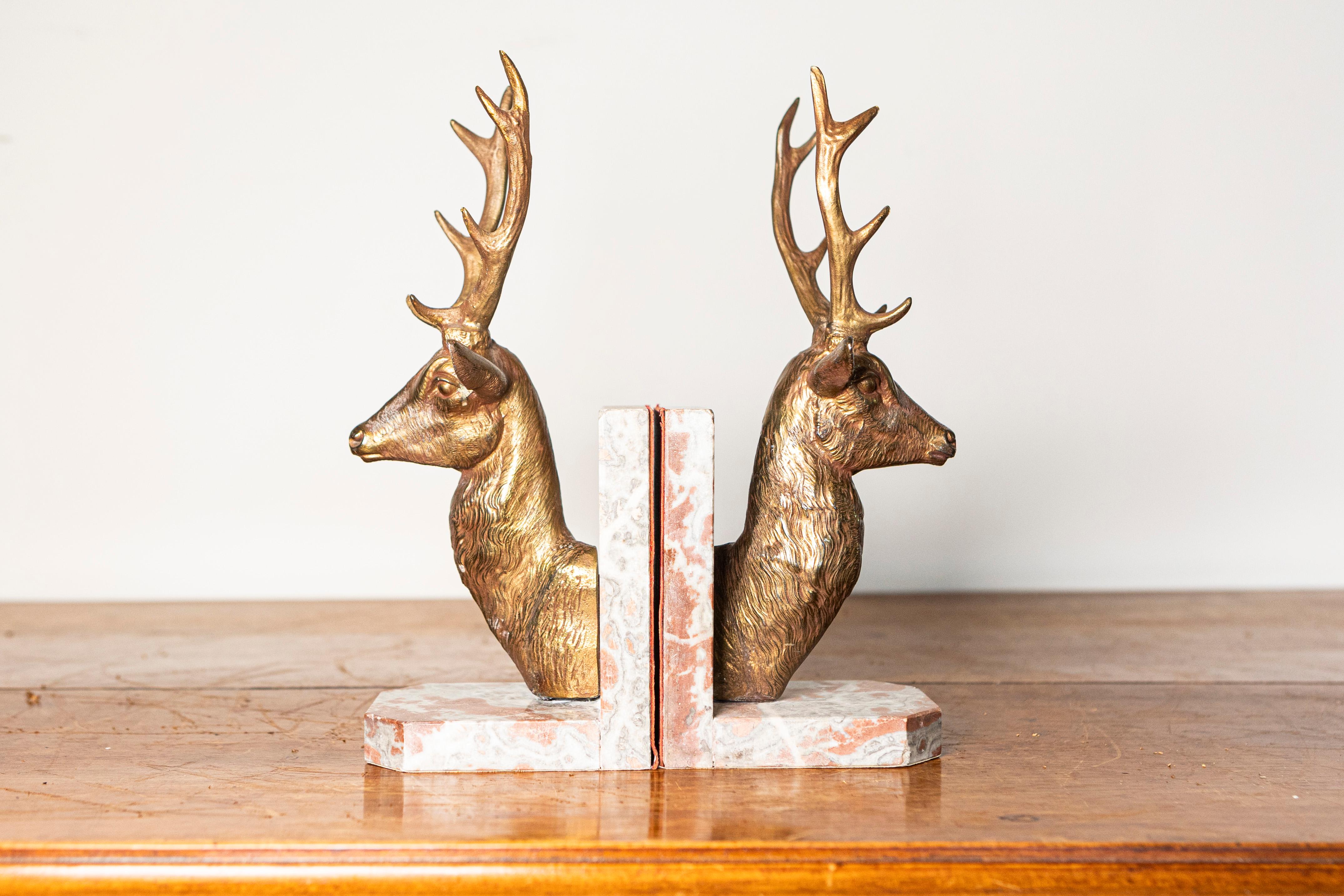 This elegant pair of 20th-century French bookends features striking stag busts crafted from gilded metal, set atop substantial veined marble bases. The finely sculpted deer heads showcase impressive antlers and beautifully textured fur, capturing