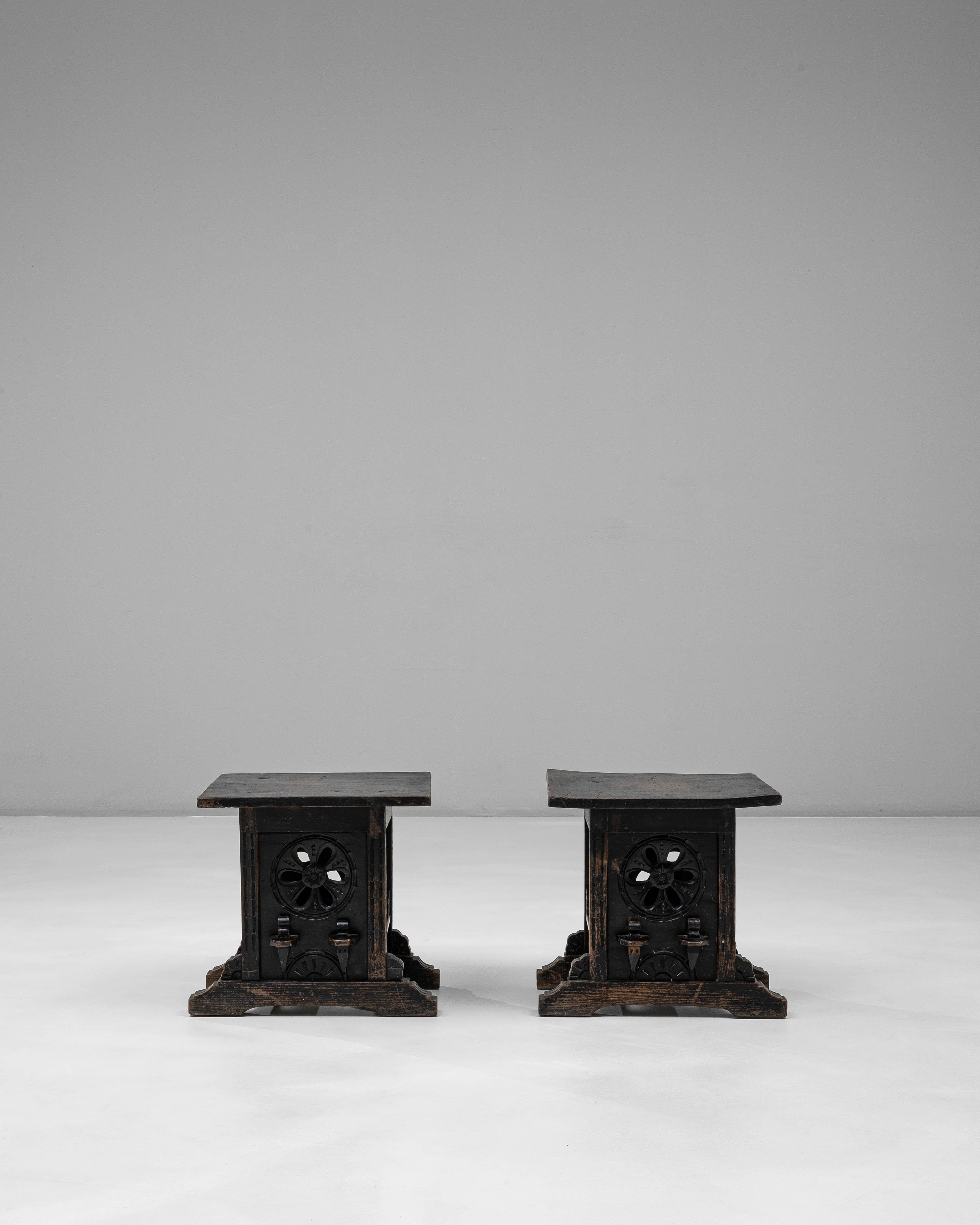 Dieses Paar schwarzpatinierter französischer Holzhocker aus dem 20. Jahrhundert zeichnet sich durch seine architektonische Präsenz aus und verbindet rustikale Handwerkskunst mit gotisch inspirierten Details. Jeder Hocker besteht aus einer