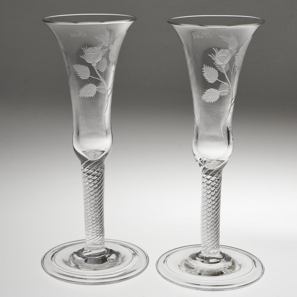 Heading : Pair 20th century Georgian style Jacobite champagne flutes
Period :  George V - c1935
Origin : England 
Colour : Clear with grey hue
Bowl : Waisted bell - Engraved with a rose, one open and one closed bud with an oak leaf and the motto
