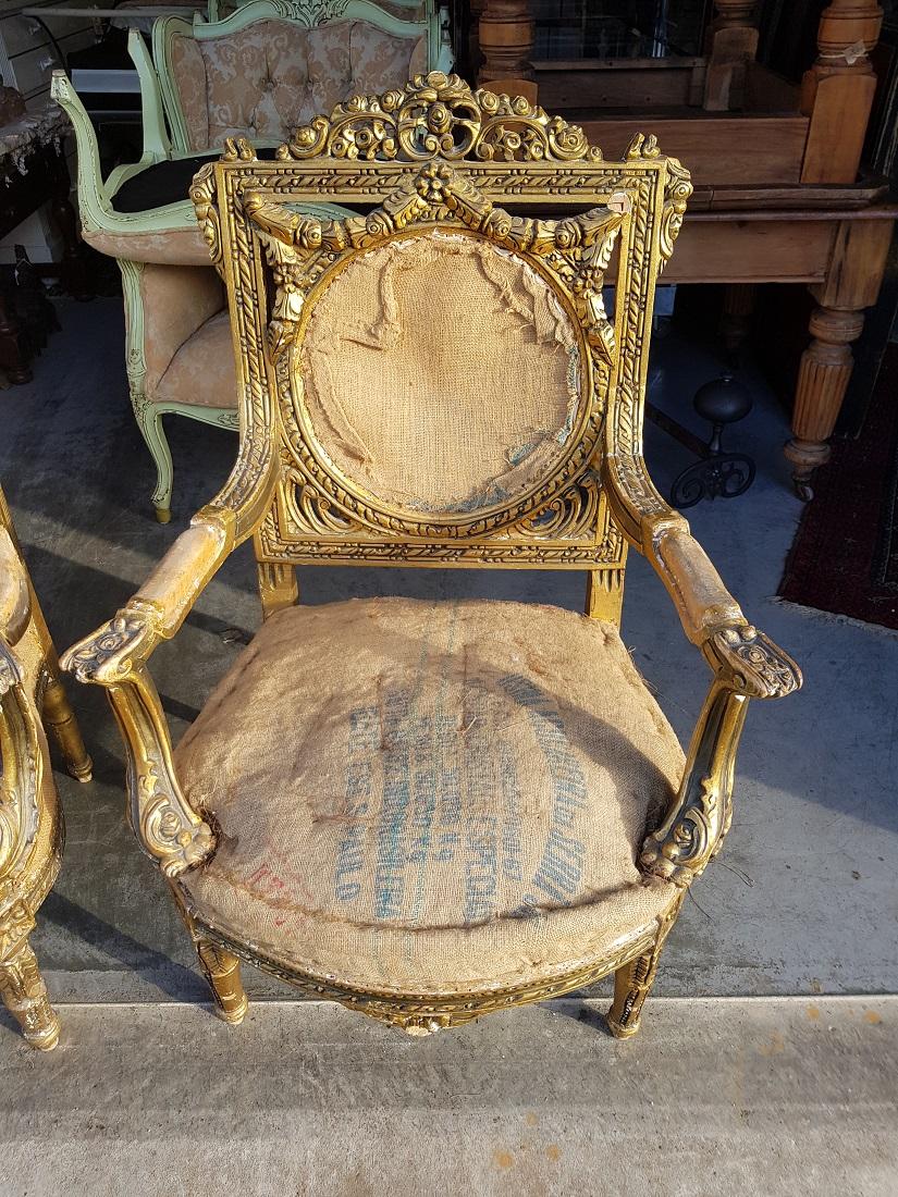 Set of 2 gilt wooden armchairs in Louis XVI style with carving all around and raised with plaster after which gilt, both are stripped of upholstery and can be re-upholstered almost as quickly, both are in a reasonable condition with some wear marks