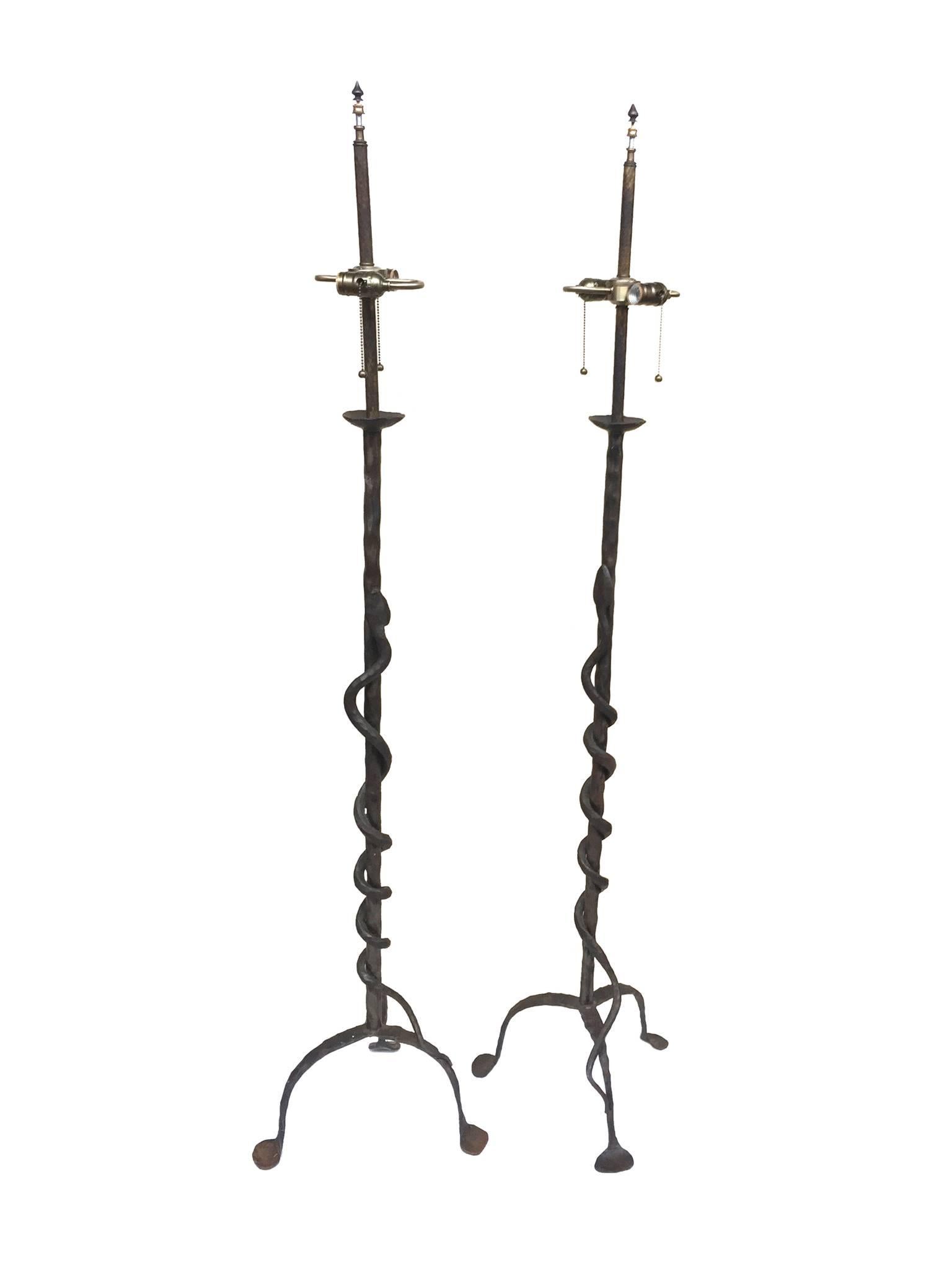 These floor lamps are comprised of hand-forged iron with. Their most striking feature is a coiled snake design, which wraps around the pole and winds down to the three-legged base. The lamps are newly rewired with new brass hardware. Each lamp can
