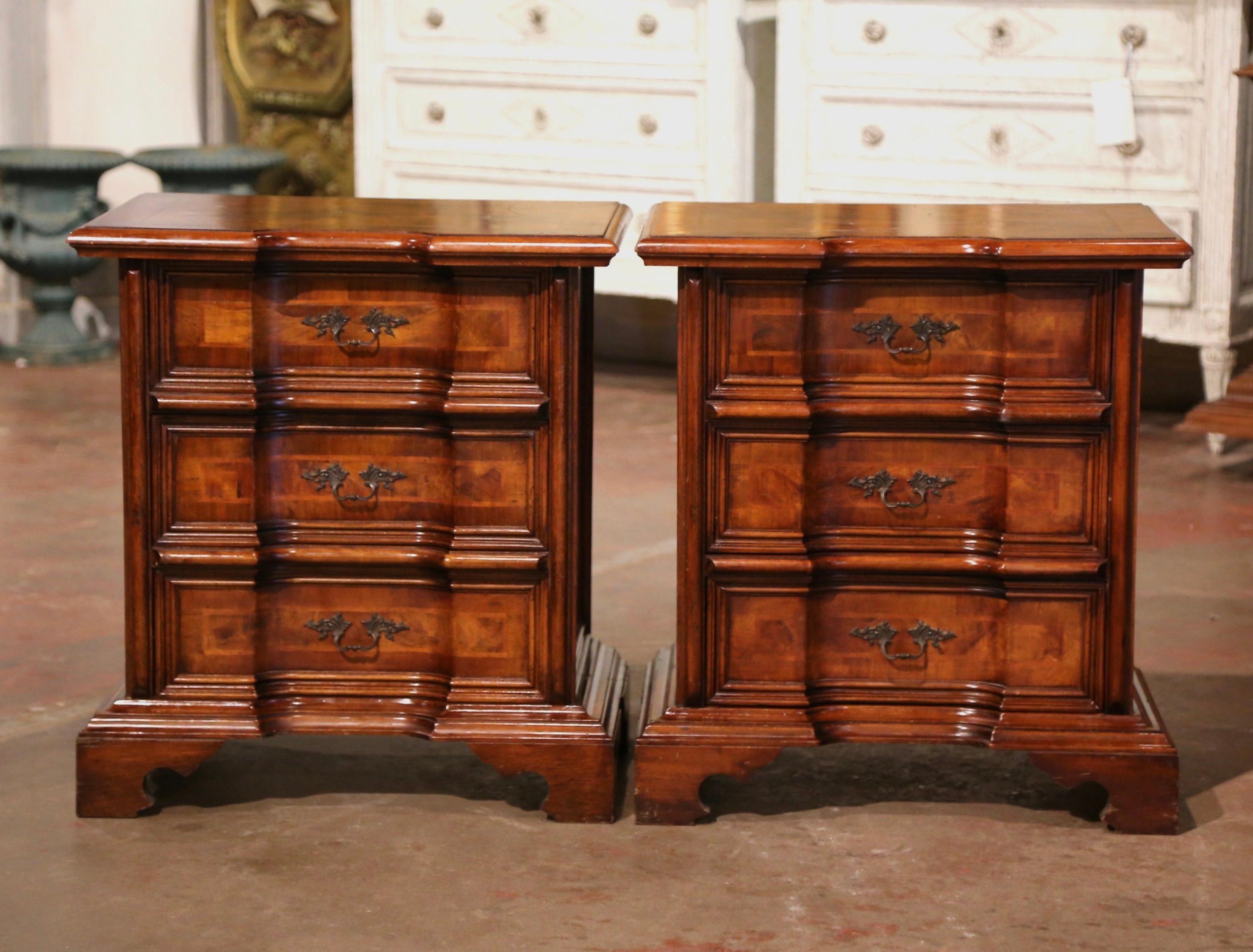 Decorate a master bedroom with this elegant pair of antique nightstands. Crafted in Italy circa 1970, each chest stands on scrolled bracket feet over a canted form case. Each cabinet features three recessed drawers decorated with inlaid marquetry