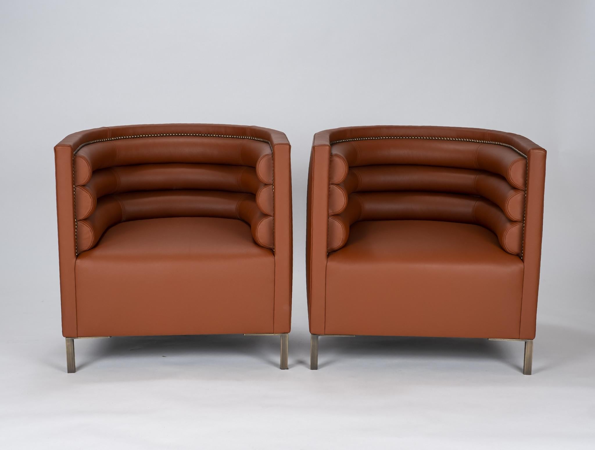 A pair of Italian channeled barrel back chairs professionally reupholstered in cognac leather with bronzed legs and nailhead detail.