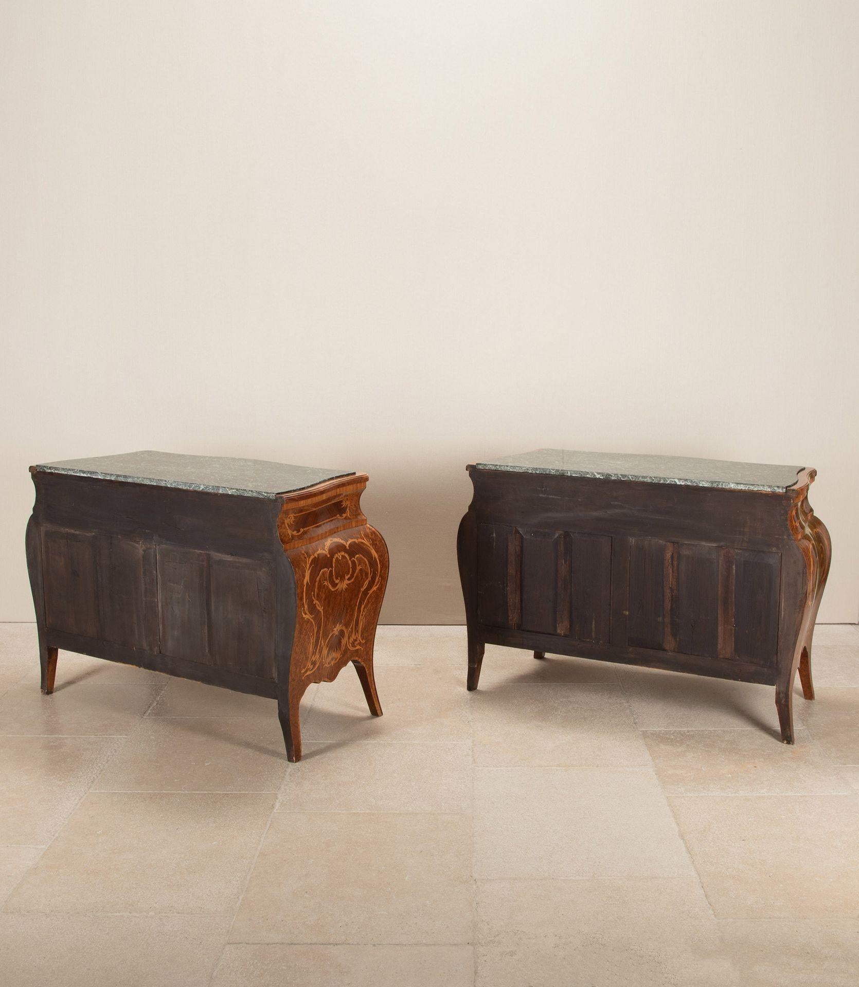 A pair of 20th Century Italian Bombe commodes featuring a display of burr walnut boxwood and kingwood.
These commodes have green and white veined marbles and are finished with their original handles.