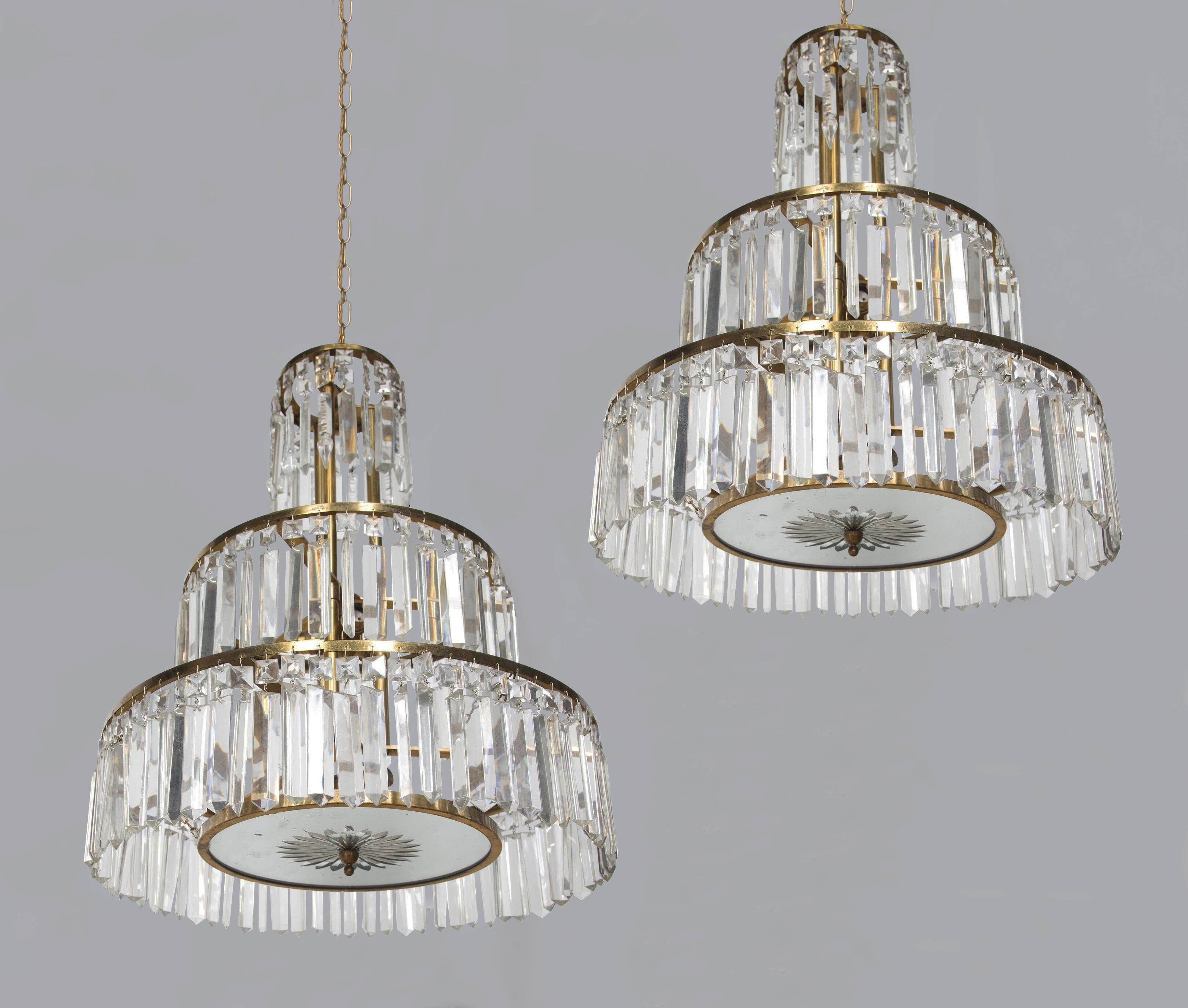 Incredibly stylish pair of matching super quality Italian mid-century 3-tier chandeliers.

With crystal prism drops hung from graduated brass circular rings ending with a circular mirrored dish with a cut glass star and brass finial. 

Chic,