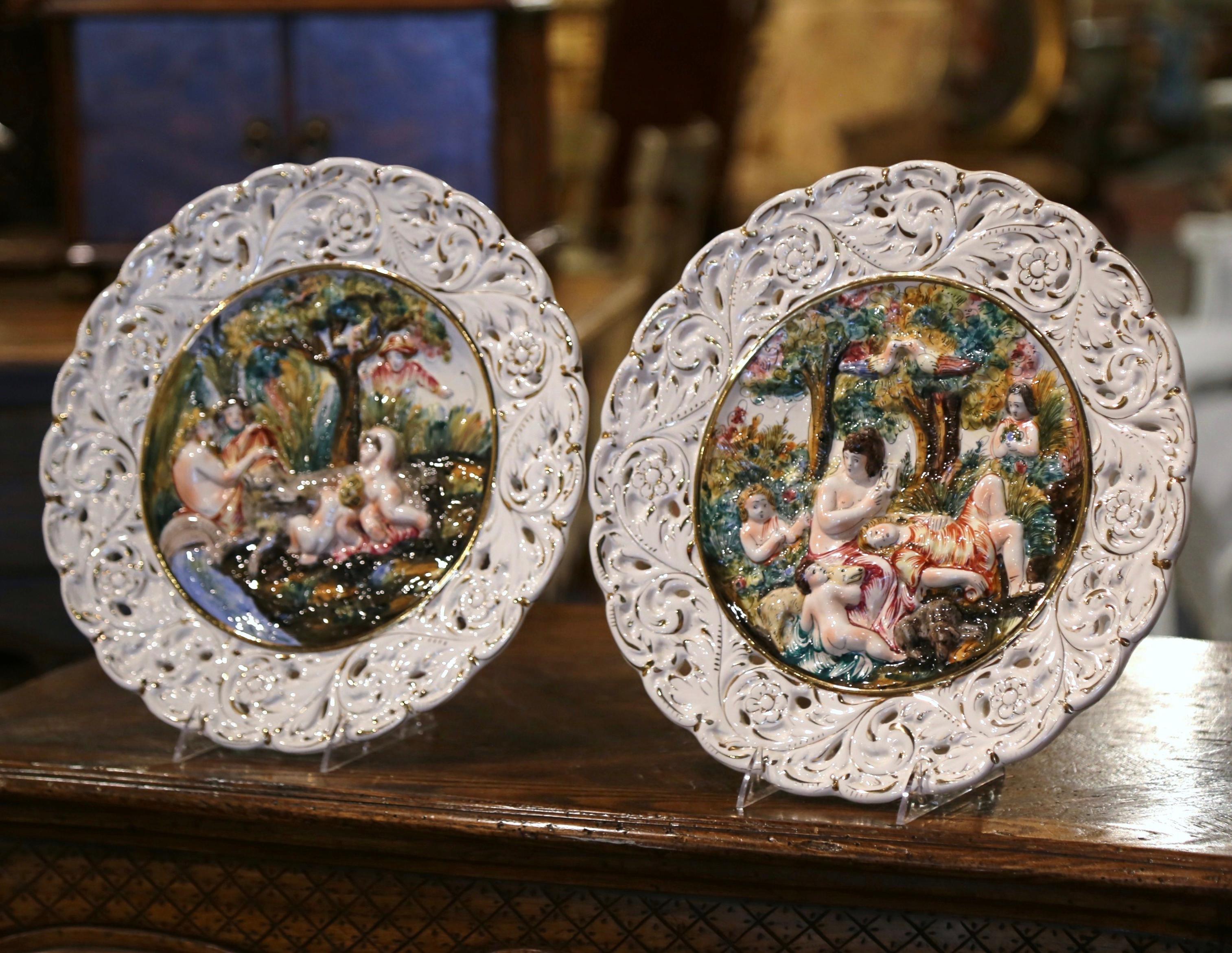 This beautiful pair of majolica wall plates would elevate any living room, kitchen, or dining room wall. Created in Italy circa 1980 and done in the Capodimonte style with high relief, each barbotine plate depicts a group relaxing in the central