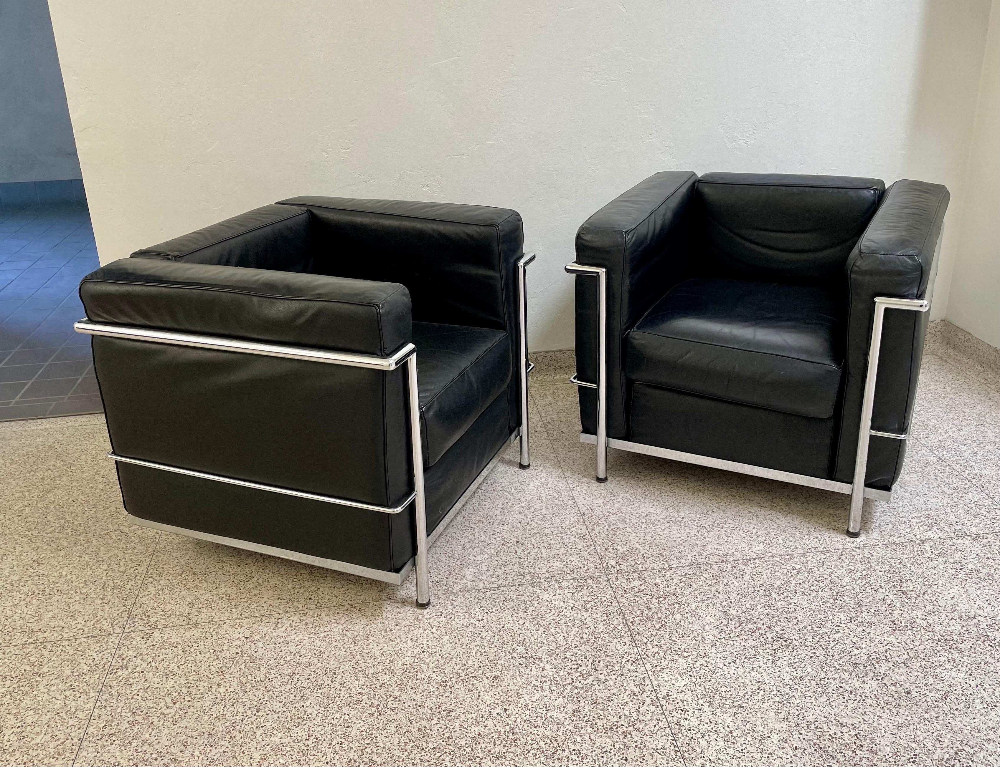 A pair of leather club chairs crafted in the iconic style of Le Corbusier, Pierre Jeanneret, and Charlotte Perriand. Manufactured in Italy by Palazzetti, circa 1970's. They are comprised of a chrome frame, black leather upholstery, and foam