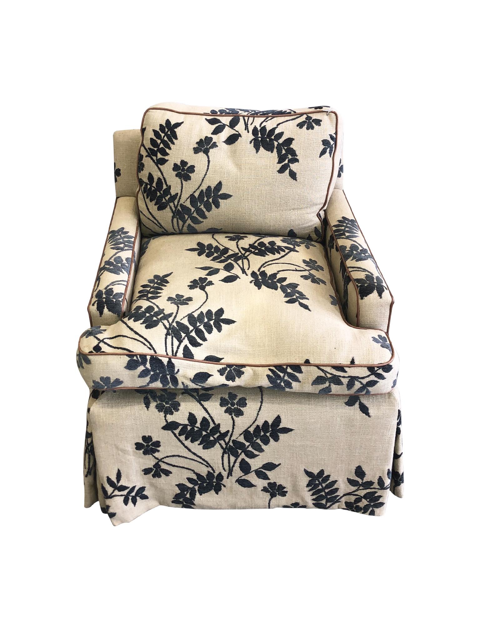 An elegant pair of lounge chairs in the Hollywood Regency style of Billy Haines, 20th century. The chairs are upholstered in a linen fabric with navy-blue embroidered botanical and floral motifs. They have a classic shape with seat and back cushions