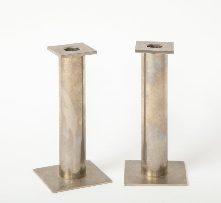 Sleek pair of modernist chrome candle holders with a clean, square base and cylindrical body.