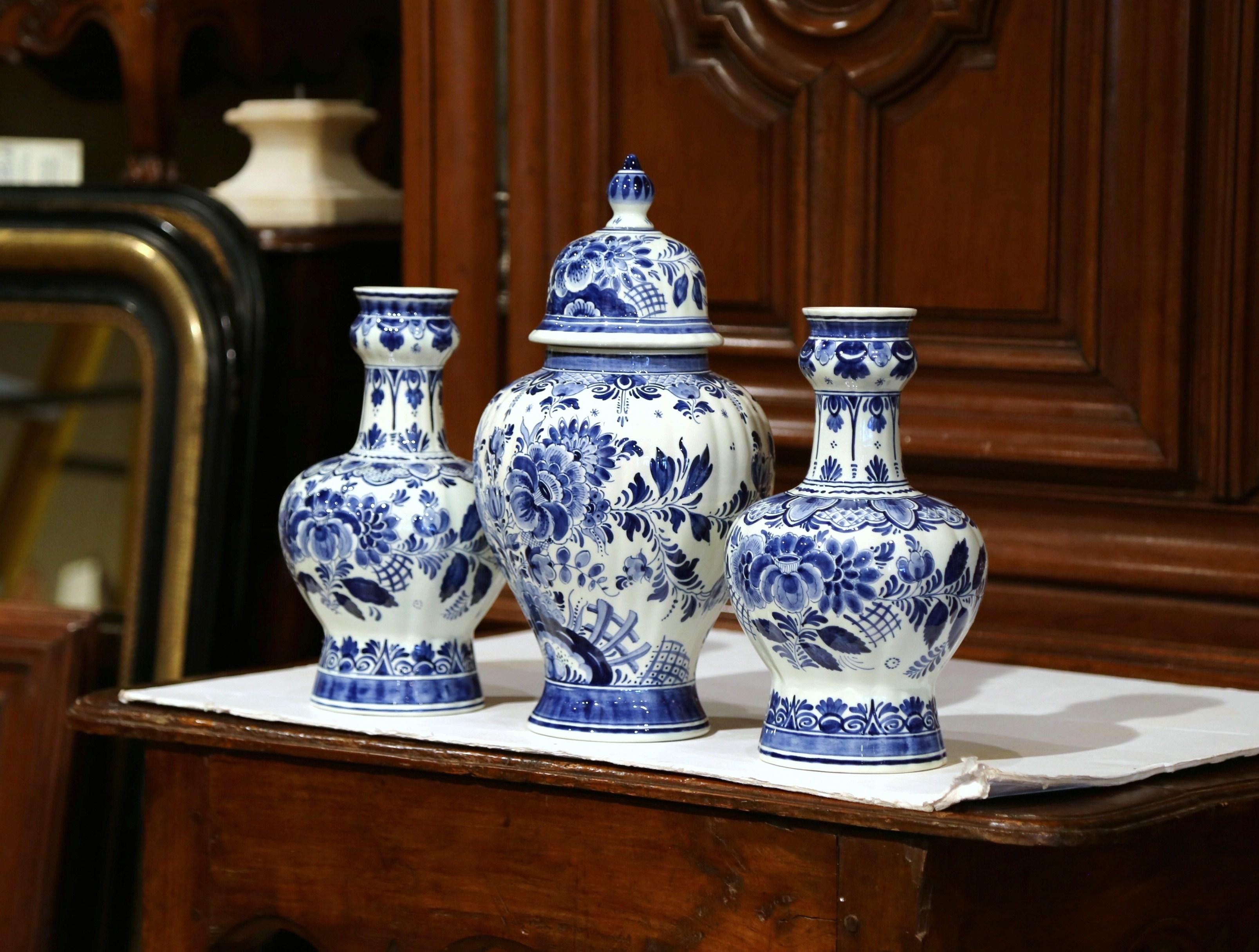 Decorate your mantel or your entry way console with this elegant set of Delft vases; crafted circa 1950, each hand-painted vase with matching jar, features floral decor in the blue and white palette. The tall ginger jar as a dome shaped lid with top