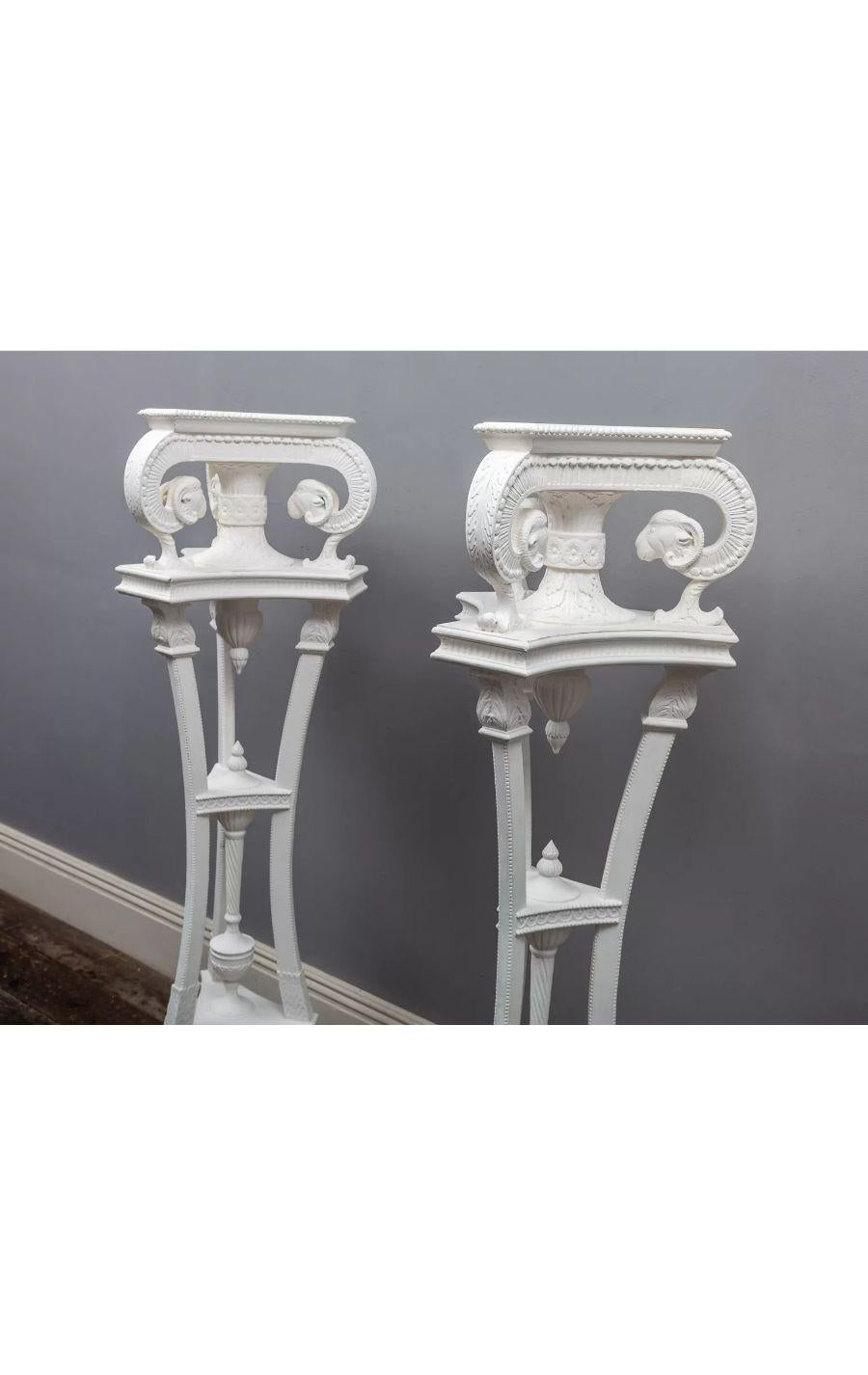 A pair of painted hardwood neo-classical torcheres in the manner of Robert Adam.

With tripartite Corinthian supports, stylised ram’s heads and cloven hoof feet on raised plinths. 

20th century.