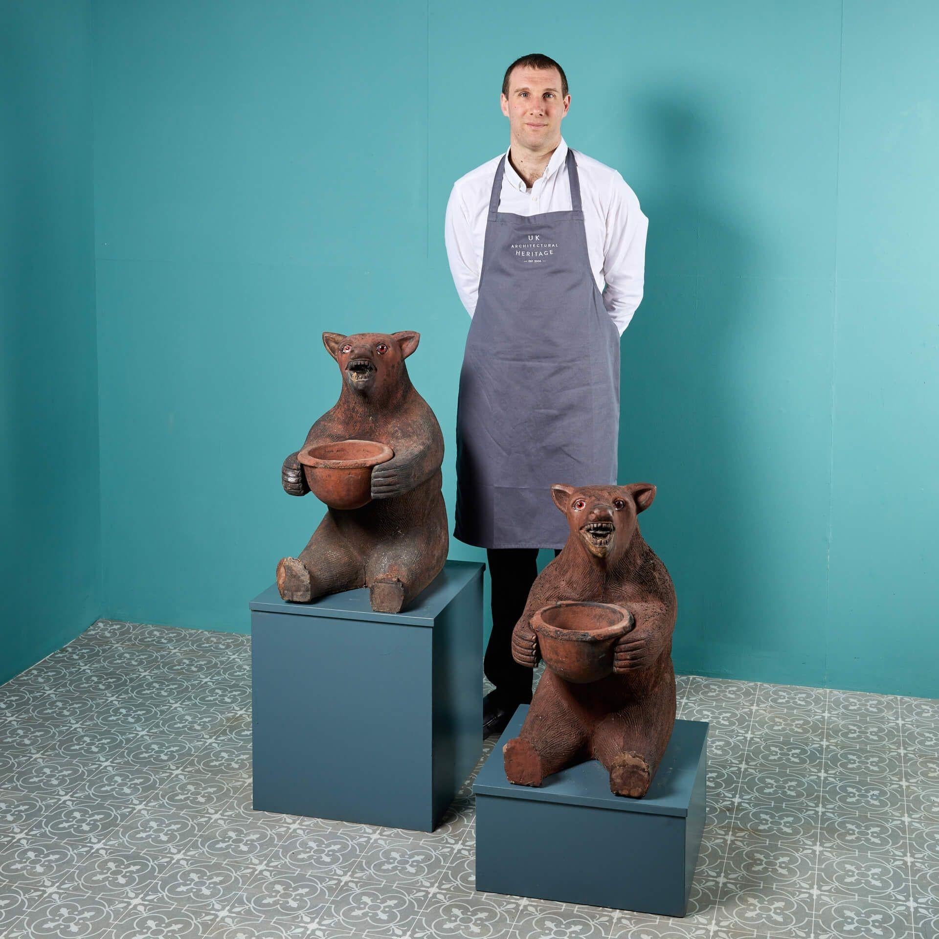 An impressive pair of early 20th century terracotta brown bear statues, each holding a detachable terracotta bowl which could be used as a planter. An amusing duo, these bear statues are characteristically sculpted in a sitting position and have