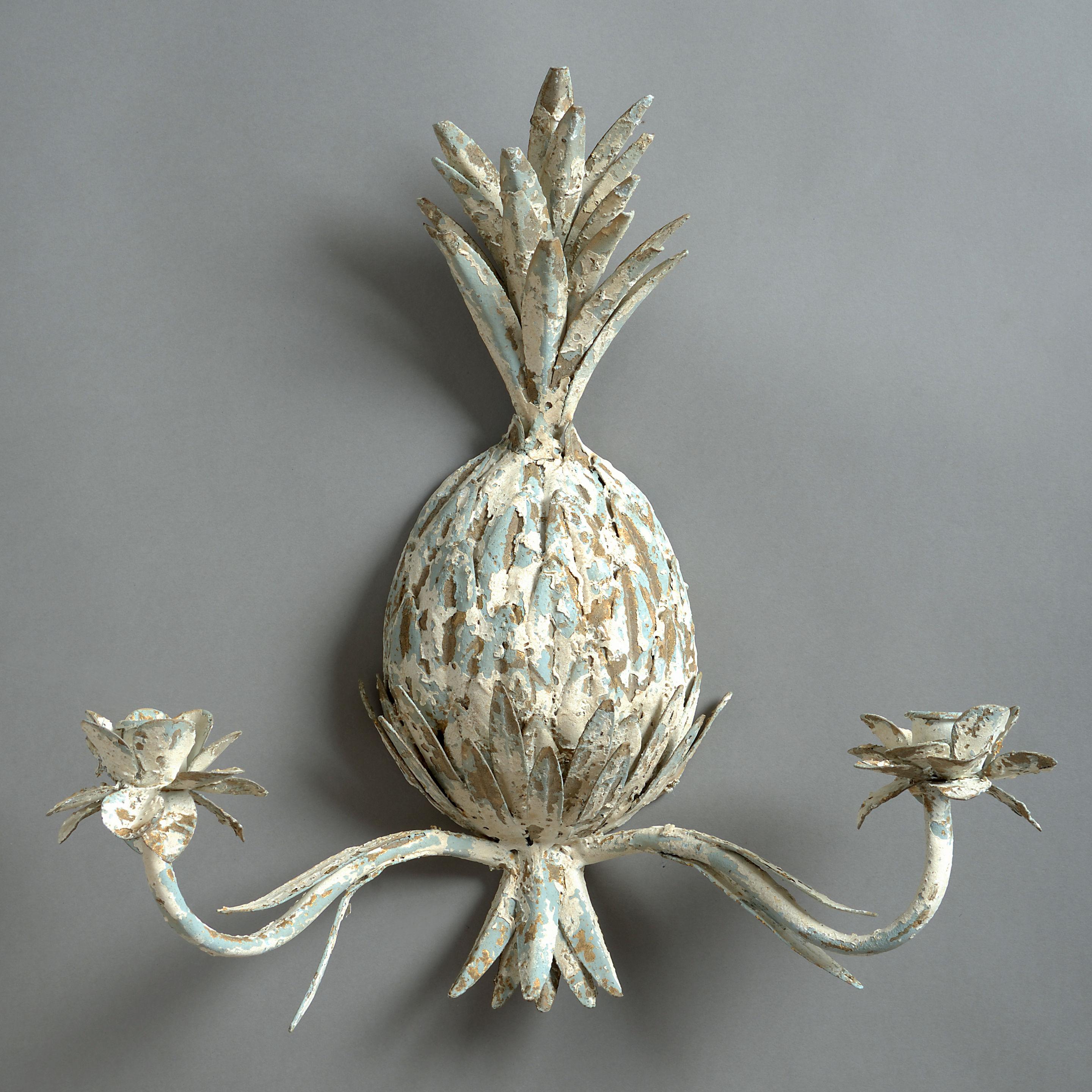 A pair of 20th century white painted tole two-arm wall lights, taking the form of pineapples. 

Traditionally, since early colonial times, the pineapple has become a symbol of welcome. The first European encounter with this fruit was by
