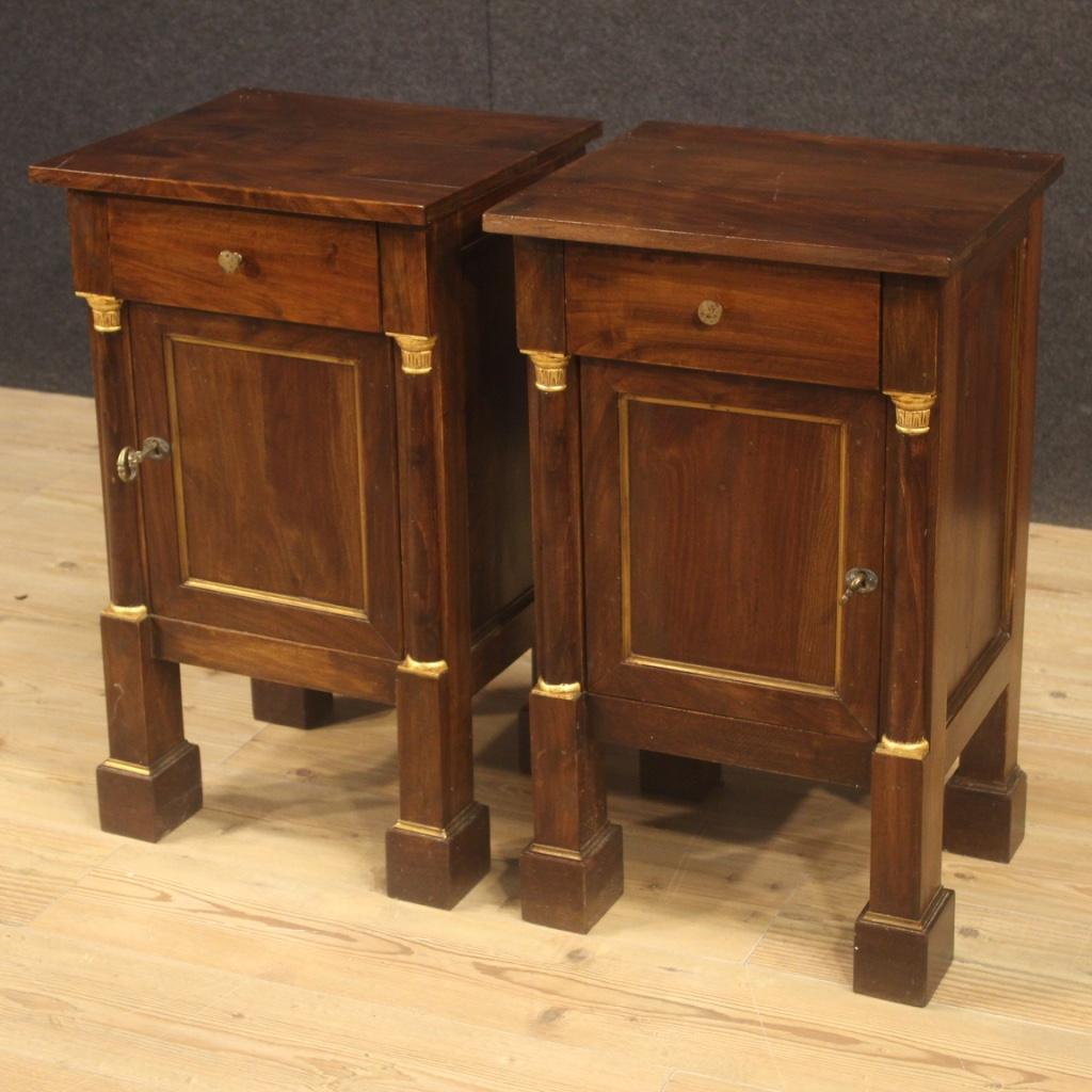 Pair of Italian bedside tables from the 20th century. Empire style furniture carved in walnut, beech and fruitwood with gilded wood and brass decorations. Bedside tables with one door and one drawer, adorned with half lateral columns, of good