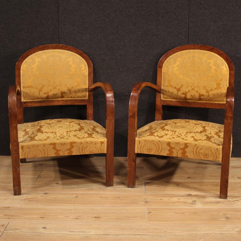 Pair of Italian armchairs from the mid-20th century. Art Deco style furniture carved in beech wood covered on the seat and back with damask fabric in good condition. Beautiful line armchairs with curved armrests and saber-shaped back feet (see