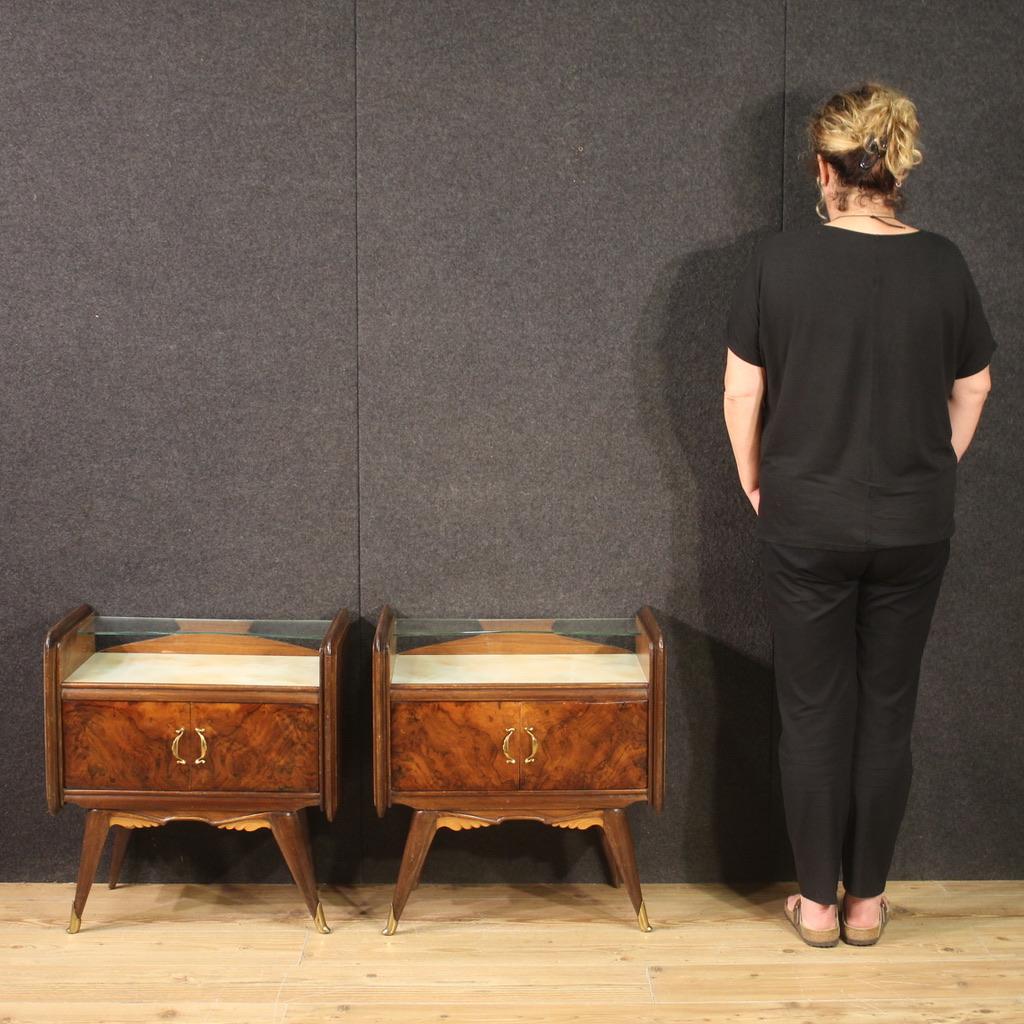 Pair of Italian bedside tables from the mid-20th century. Italian design furniture carved and veneered in walnut, burl and fruitwood. Beautiful bedside tables equipped with gilded brass handles and feet, painted glass top and second (smaller) glass