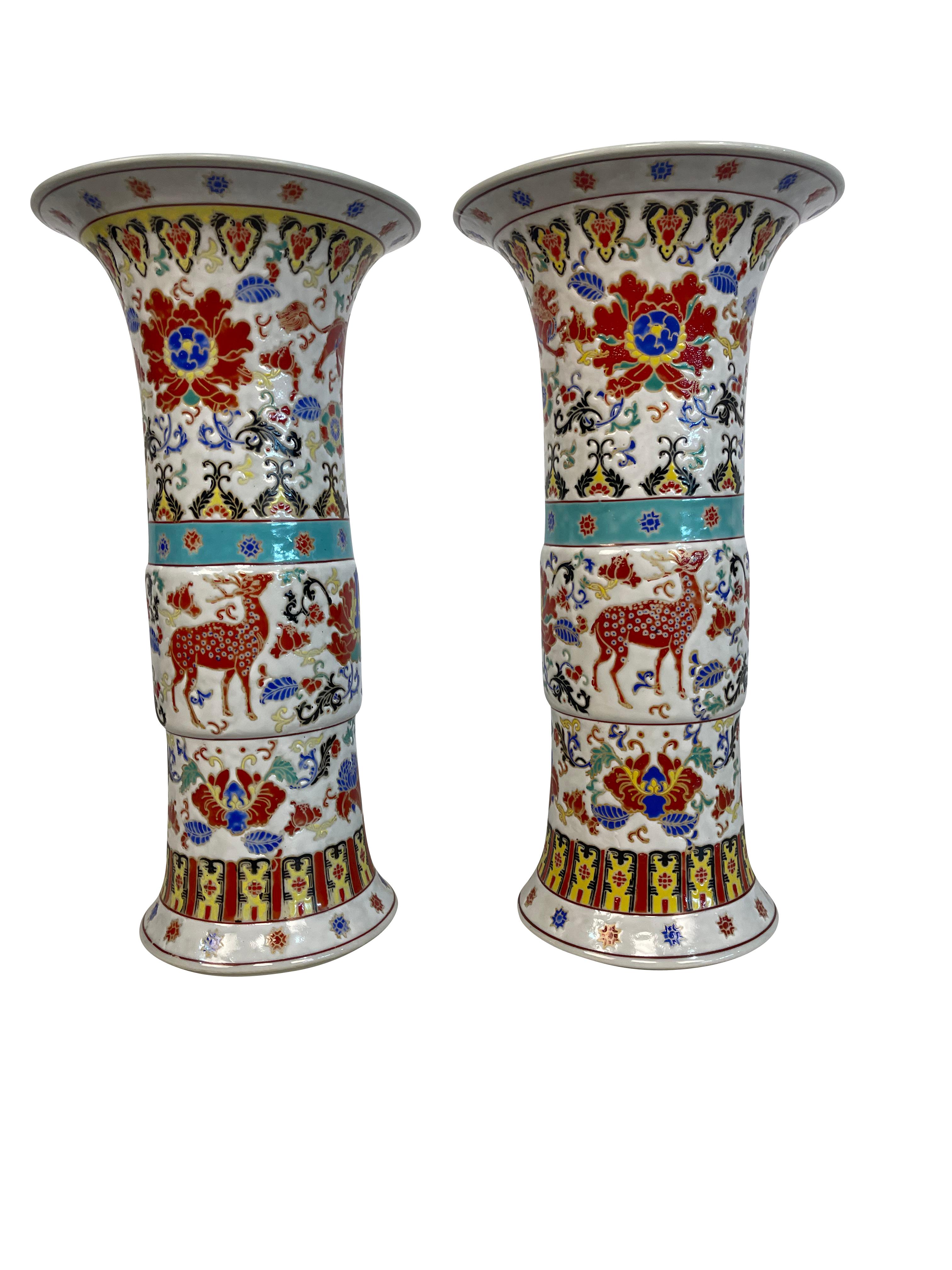 Pair of Yongzheng style Chinese porcelain vases in a high gloss finish in the Gu shape. The vases are decorated with deer, flowers, and animal motifs. Lovely shades of aqua, turquoise, blues, and rust with decorative banding at the middle and base.