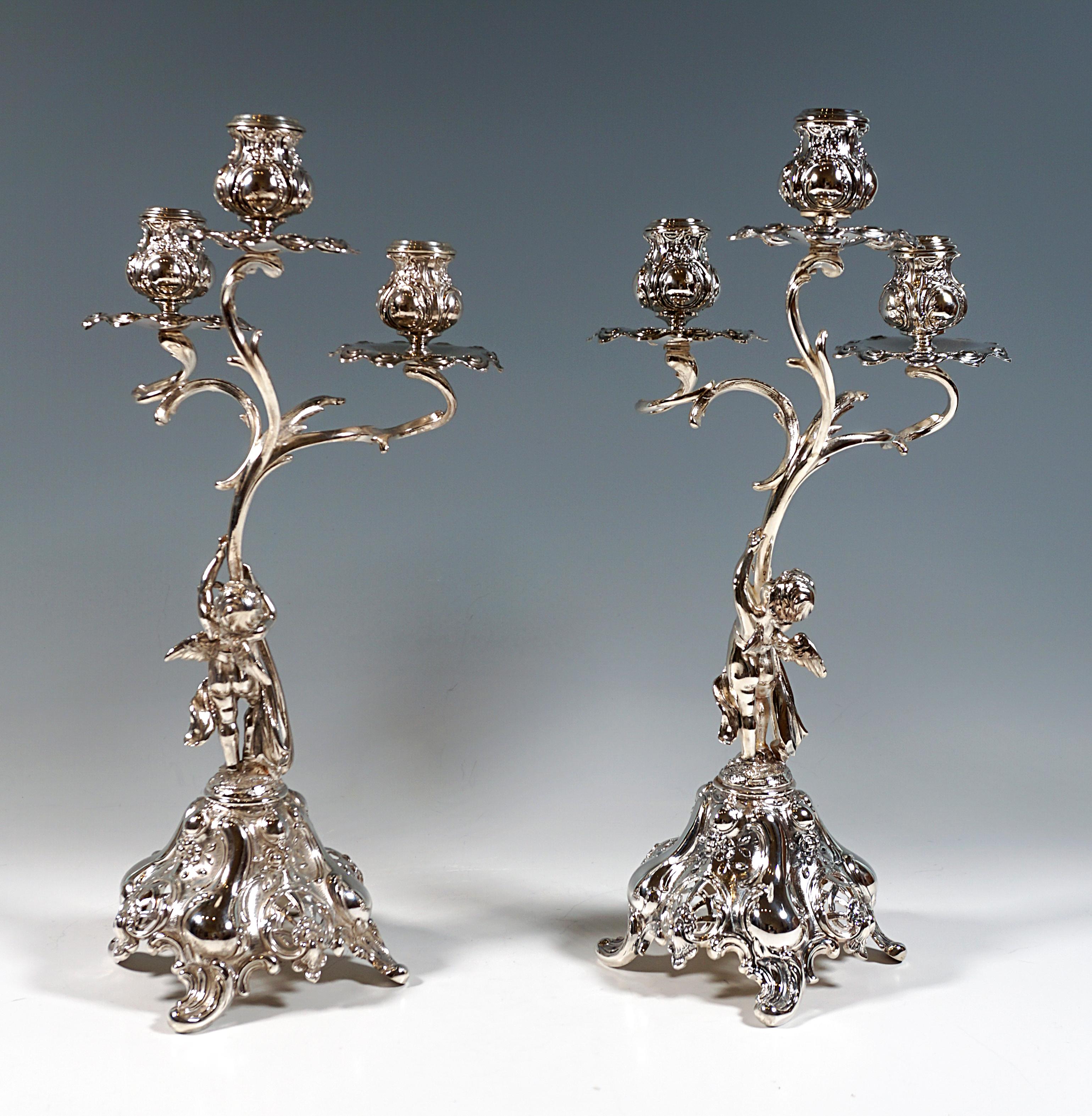 Two decorative, playful Art Nouveau candleholders on a high-towered rocaille and volute base with lattice-like pierced shells, standing on four rocaille feet in a square arrangement, on top of which are raised slender, intertwined volutes, each held