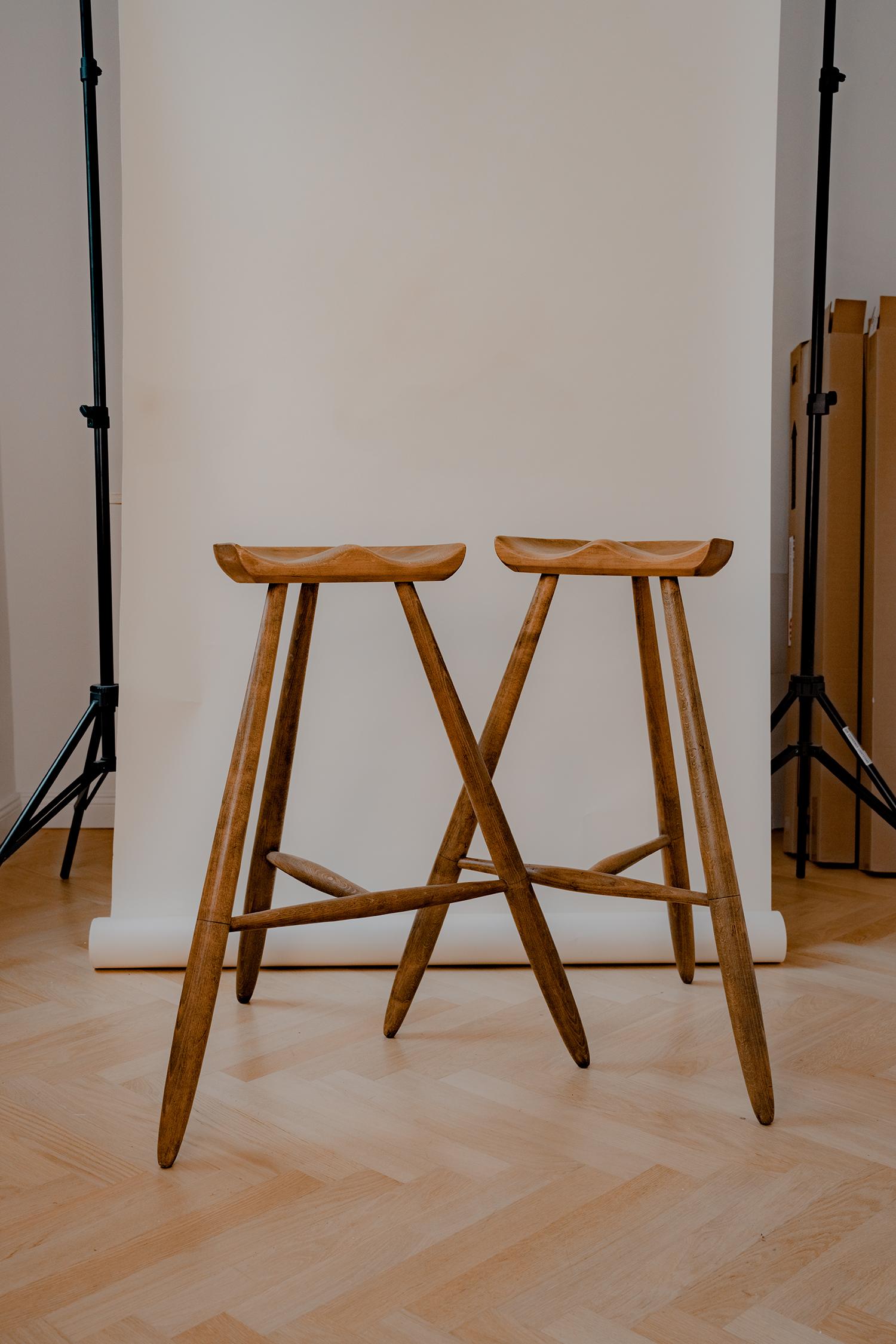 Explore our online store and discover an exceptional pairing of two very tall functional stools in the style of milking stools with three legs, designed by Arne Hovmand-Olsen from Denmark in the 1940s. These impressive stools crafted from beech wood