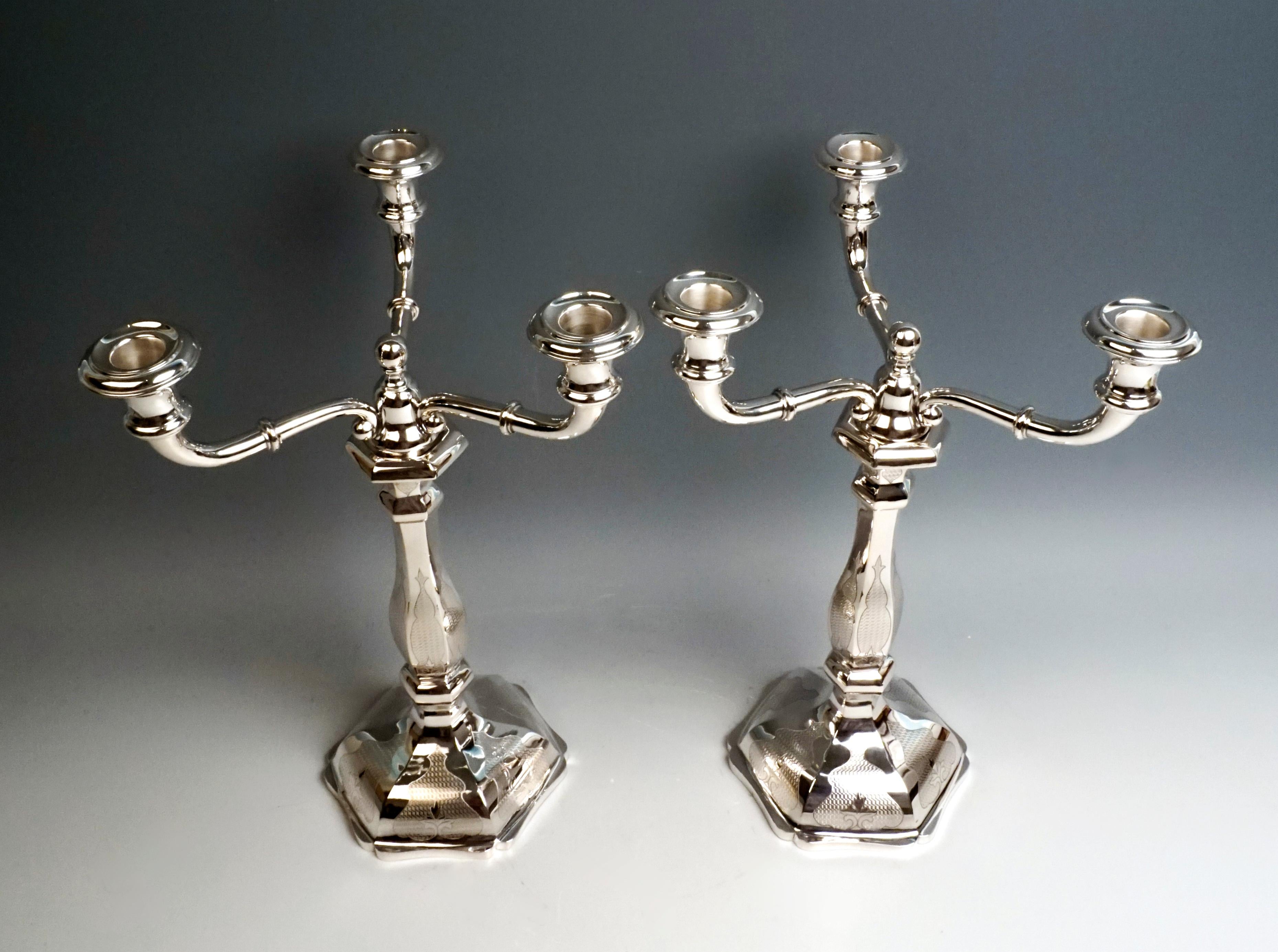 Pair of three-flame silver candelabra on a hexagonal, cambered, unfilled base. Shank with hexagonal cross-section, smooth surface with gouilloché leaf decoration. On the top piece there are three volute-shaped curved arms that widen upwards and open