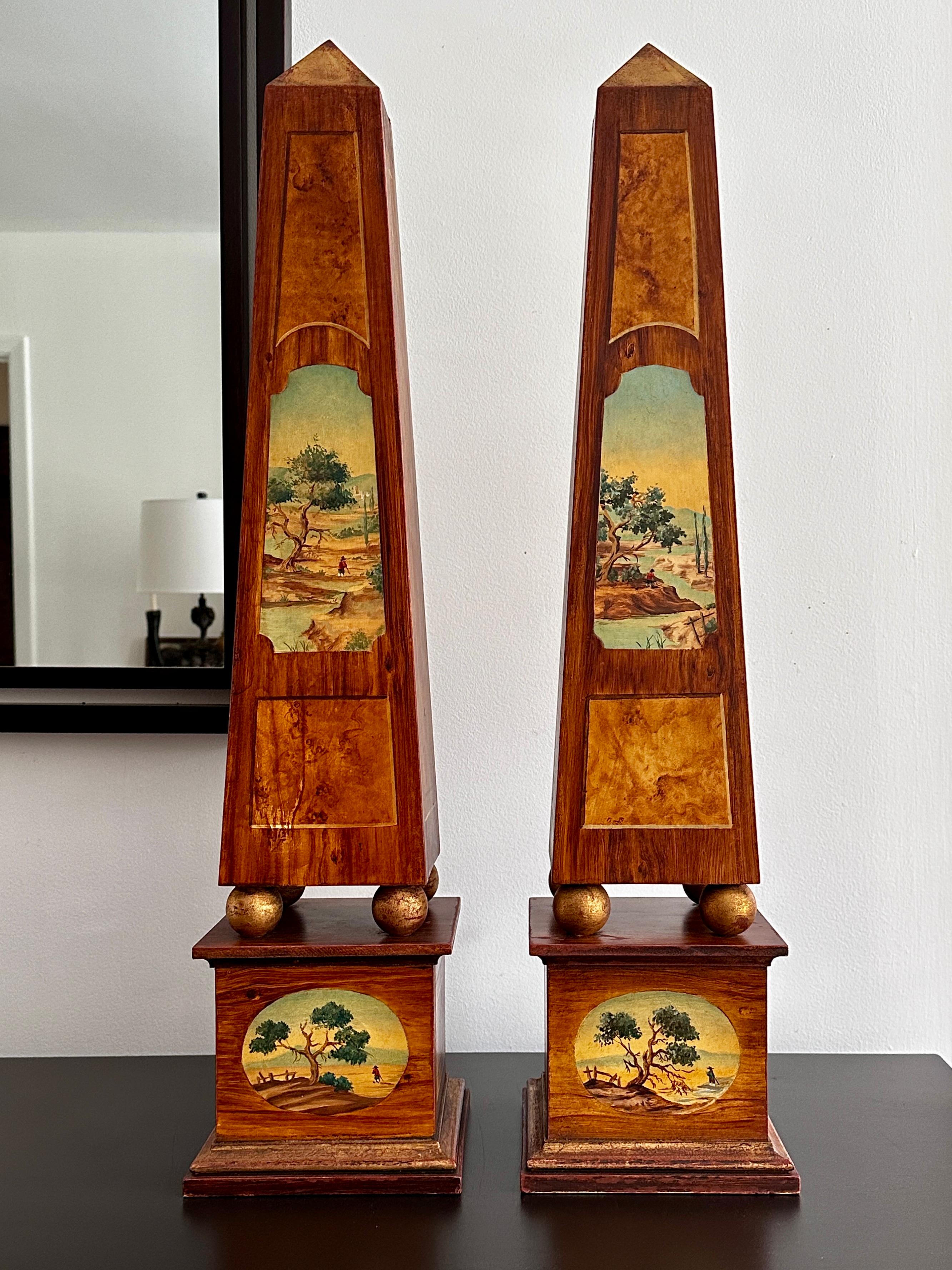 Coppia di alti obelischi in legno con finiture in faux bois, dipinti della natura e decorazioni dorate, tutti dipinti a mano. Gli obelischi hanno un'altezza di 31,1/3 pollici e una forma quadrata di 7,1/3 pollici alla base, quindi sono di dimensioni