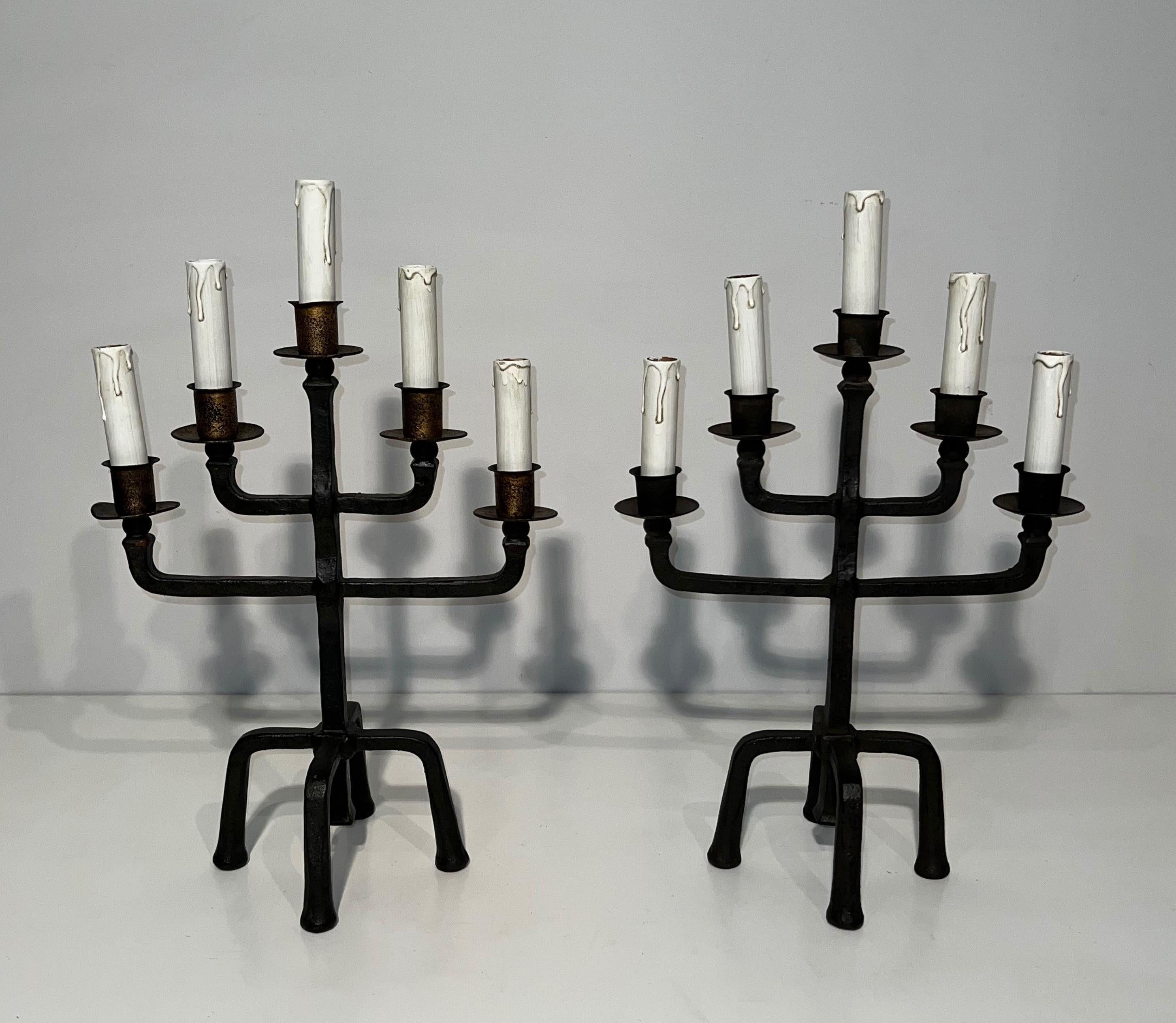 Questa bella coppia di candelabri a 5 bracci è realizzata in ferro battuto patinato e dorato. Possono essere collocati in una casa molto contemporanea o moderna, così come in un castello gotico. Questa è un'opera francese. Circa 1940