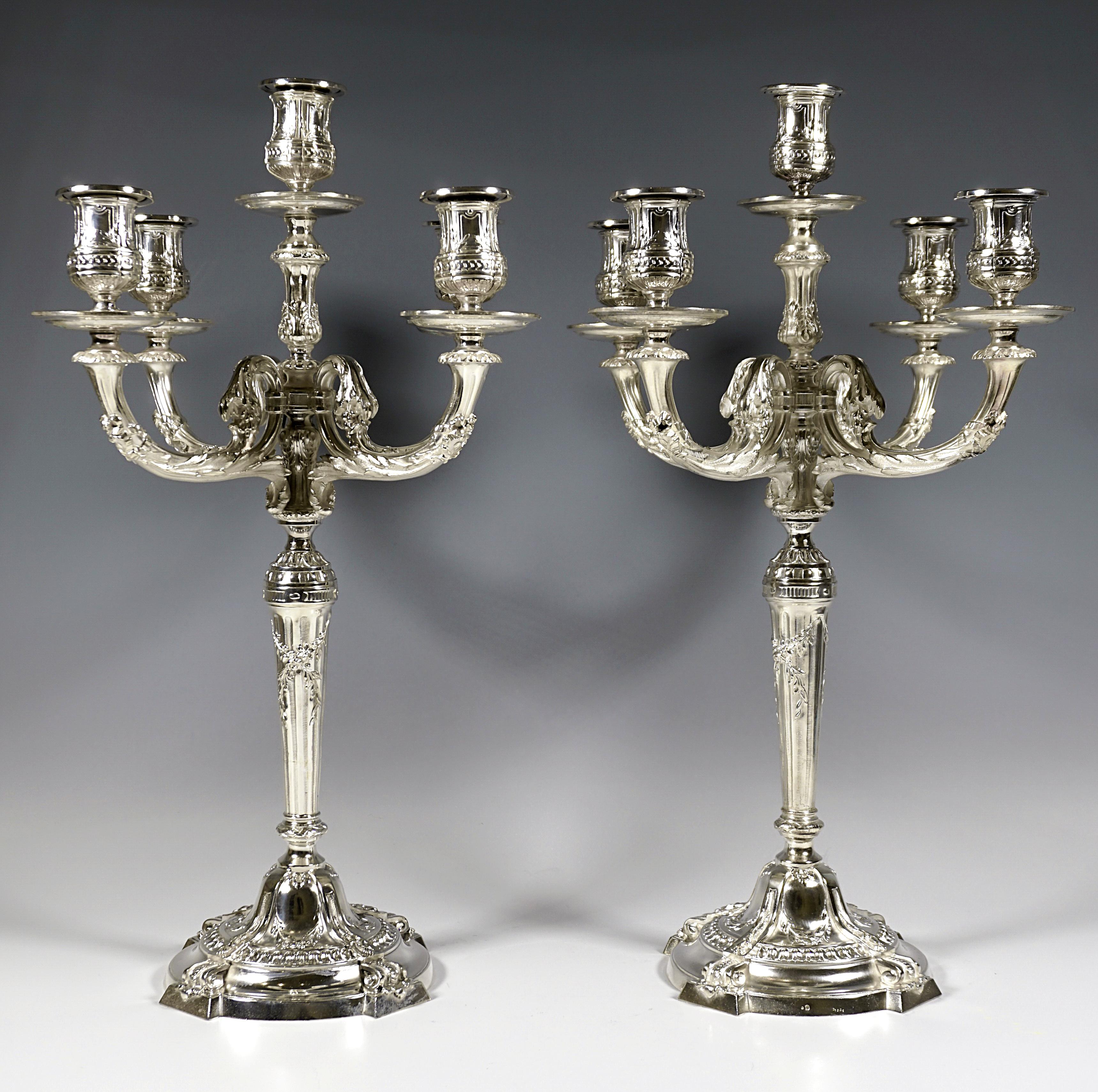 Two festive five-flame candelabras on a round, centrally raised foot, segmented by four applied pilasters with volute ends protruding over the rim, ring-shaped and radial relief bands, fluted shaft with leaf and flower festoons widening conically