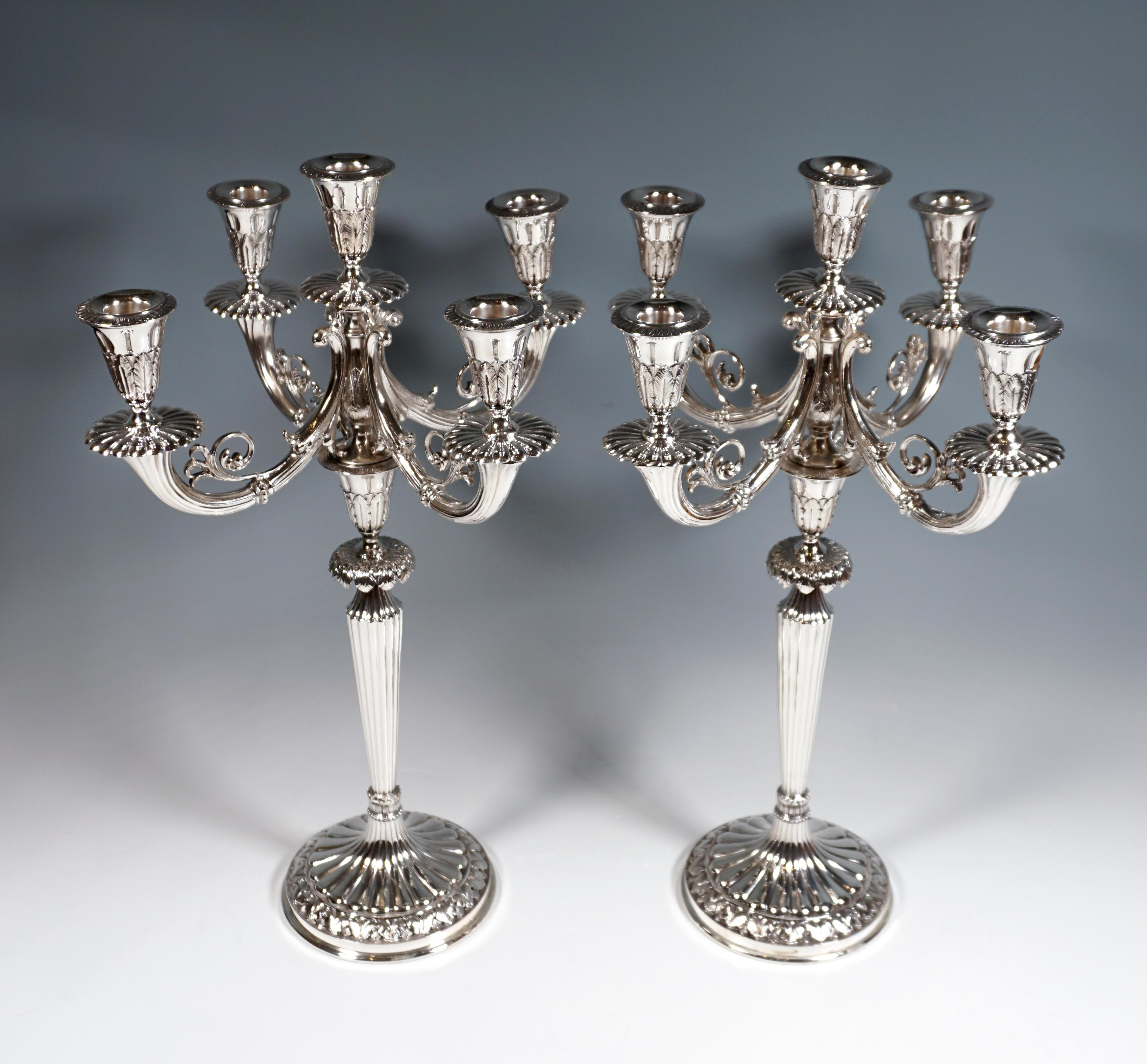 Two five-light candelabras on a round base with a leaf rosette and a raised hump decoration in the middle, bundled by a beaded band and stylized acanthus leaf tips, the hump decoration continued on the shaft that widens conically upwards,
