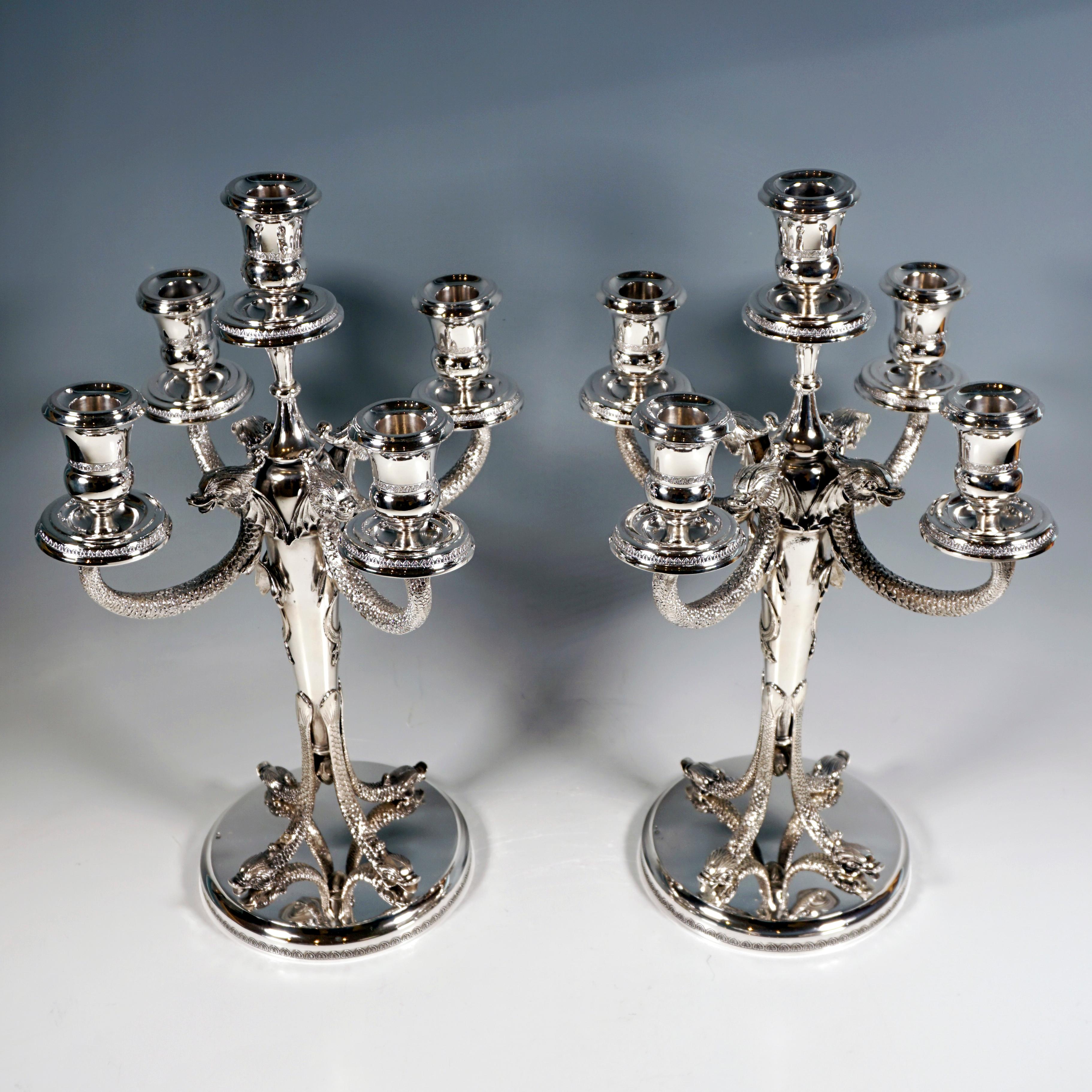 Two solid five-light candelabras, mounted on a round, fluted stepped base with a delicate palmette frieze on the side, four slender, four-pointed dolphins with their heads resting on the ground with 
their fins pointing up and supporting the