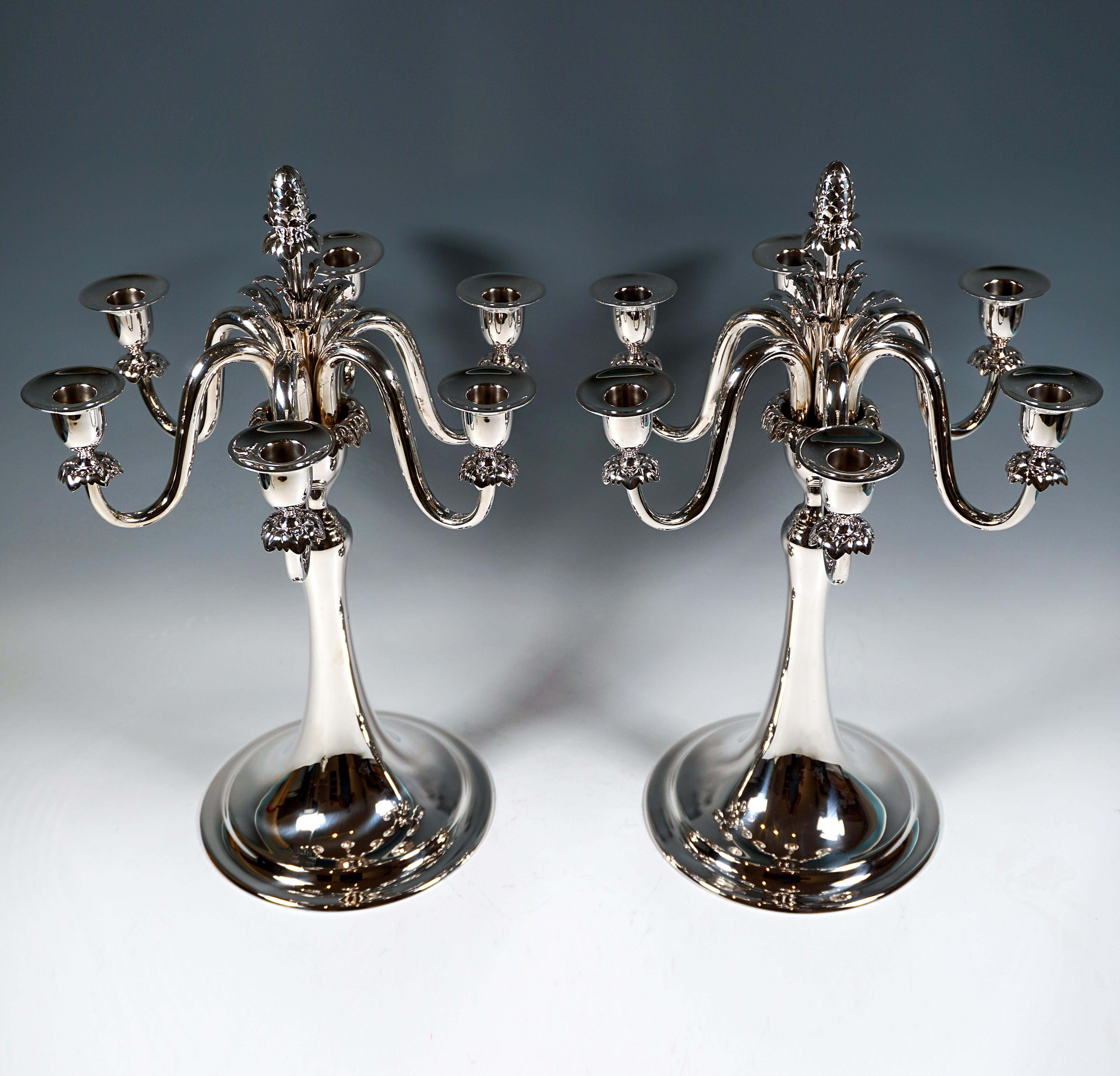 Elegancia sencilla con ese algo especial: dos candelabros de seis llamas sobre una base redonda y lisa con borde escalonado estriado, fuste elevado en forma de trompeta, cáliz formado tras la constricción con borde de punta de hoja de acanto