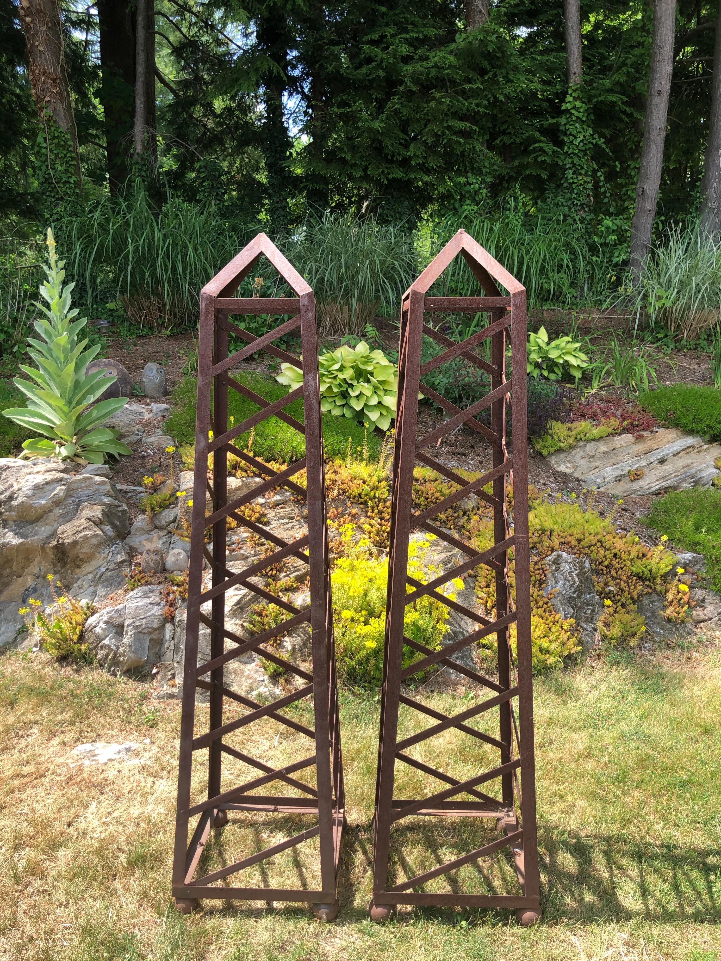 Pair of 6 Ft high vintage iron garden obelisks. Perfect to flank your front door or your garden entry. Classic design and style. Heavy well made objects of beauty. Natural wear and rust from being outside. 
This listing is for a pair/set of two.