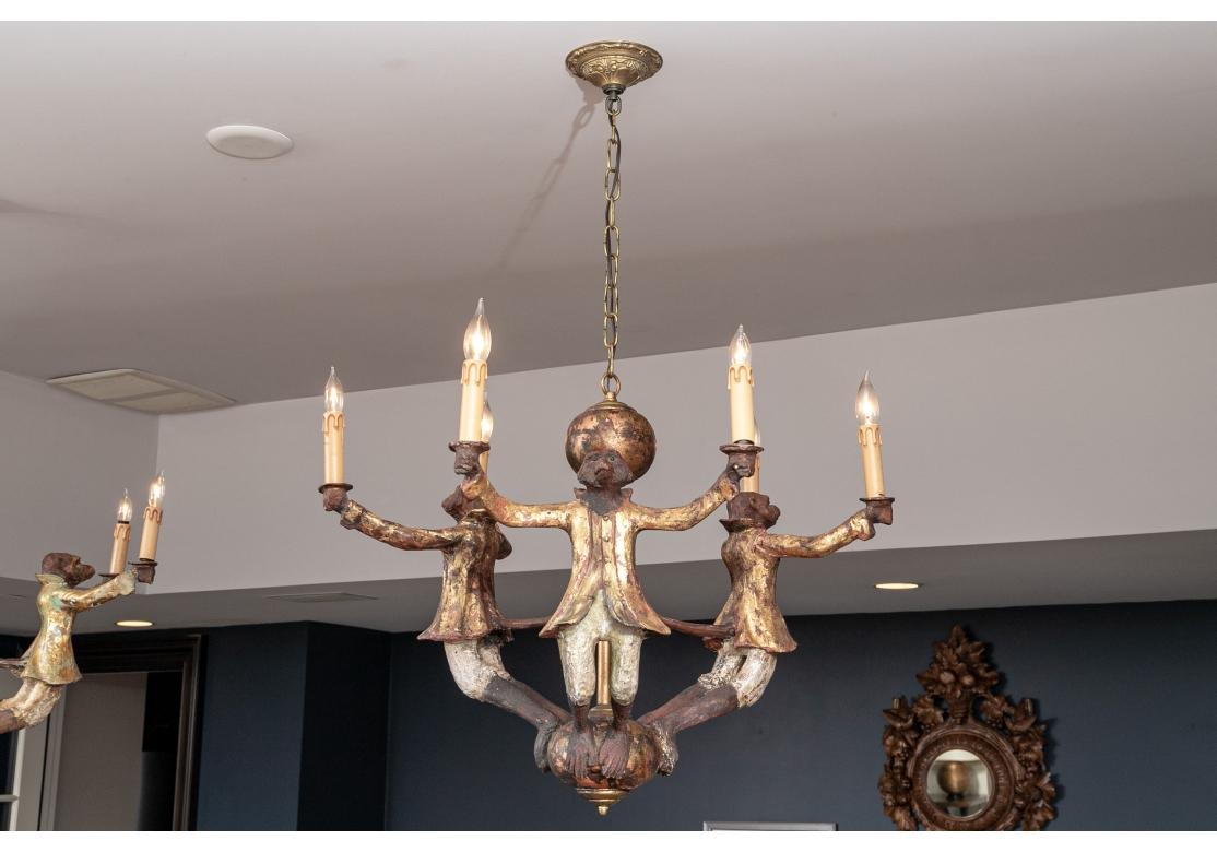 A Whimsical pair of chandeliers displaying 3 monkey form arms, each holding two candles, in the manner of Bill Huebbe. Each chandelier has a distressed gilt finish. 
Each fixture measures :30.5