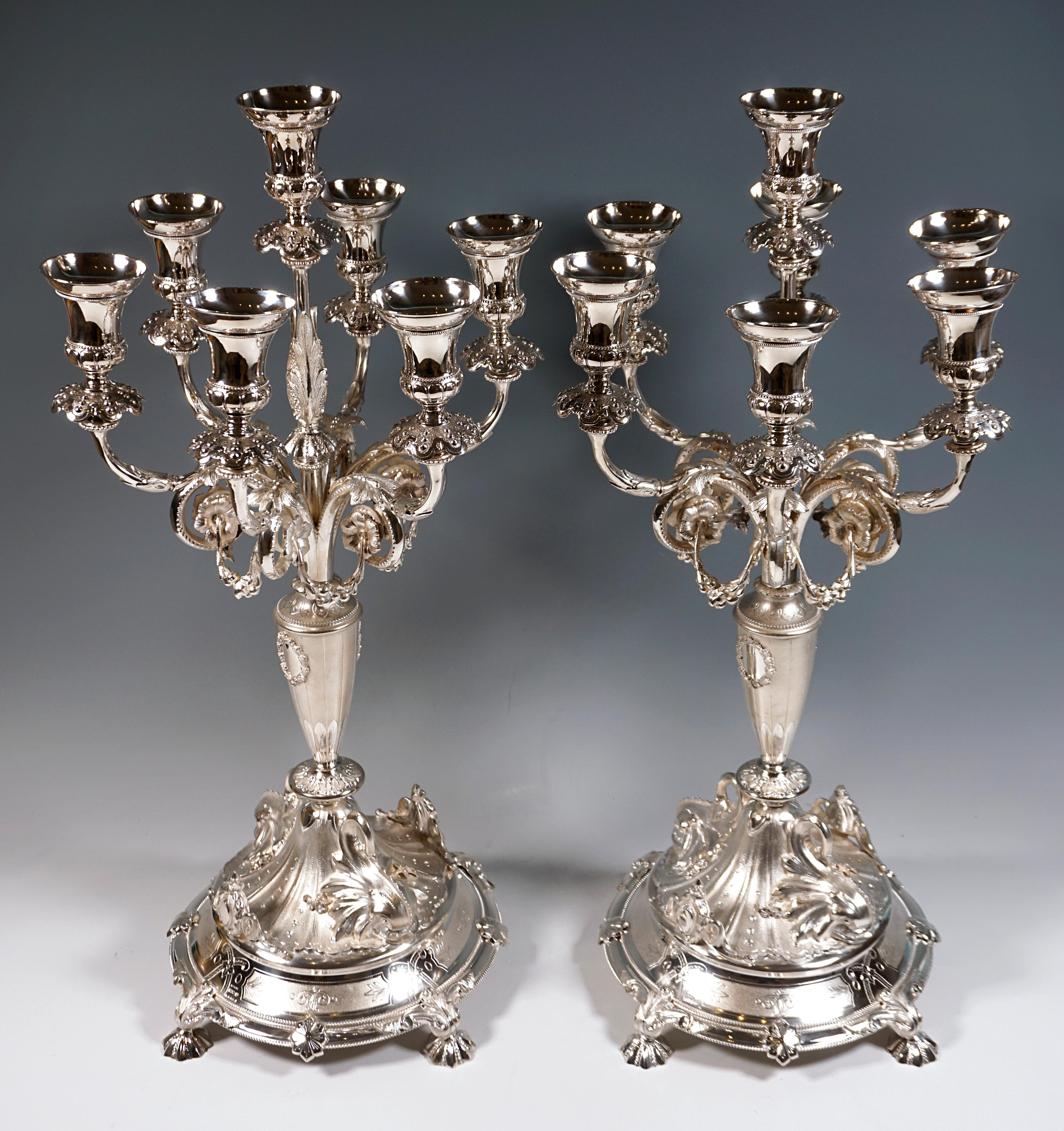 Pair of festive silver girandoles on projecting circular stand with four star-shaped feet, raised two-tiered foot with applied dolphins and cartouches, baluster-shaped shaft with six candelabrum arms with down-turned volutes decorated with flowers