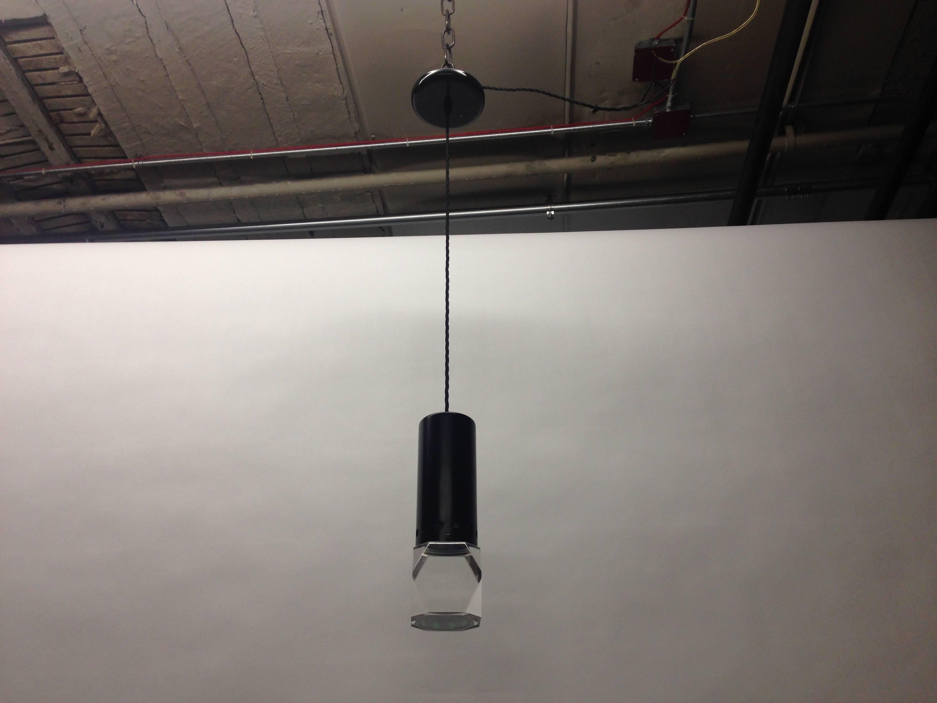 Pair of ceiling lights with thick, angularly cut clear acrylic blocks and cylindrical, black enameled metal hardware that has perforations along the bottom rim. Each light hangs from black curly wire, a black round canopy, and one candelabra socket.