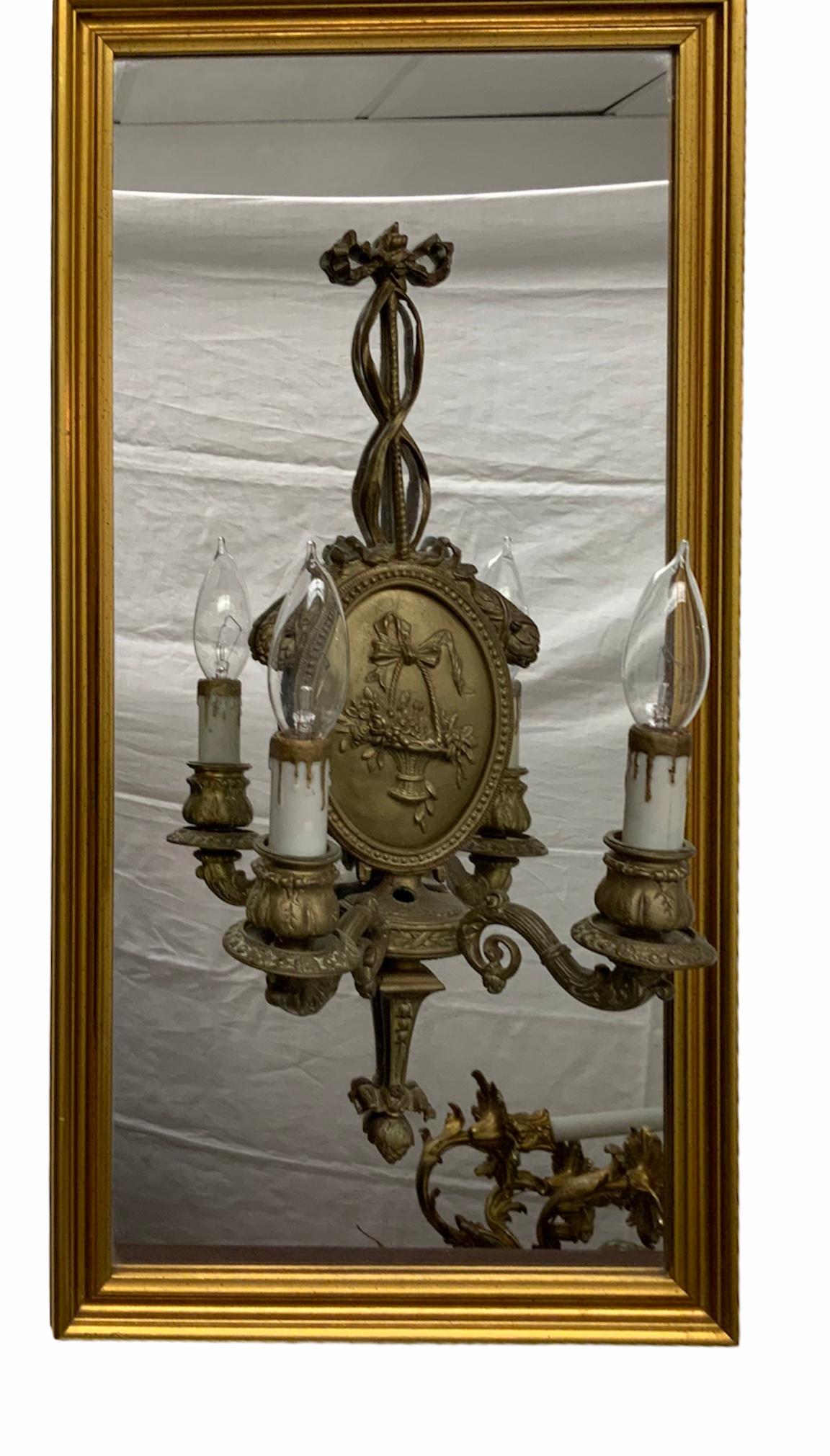This is a pair of gilt bronze Adam style two lights wall sconces. They are attached to a rectangular gilt wood framed mirrors. They depicts an oval plaque in the center that is adorned with a repousse of flowers baskets. Also bows, ribbons and
