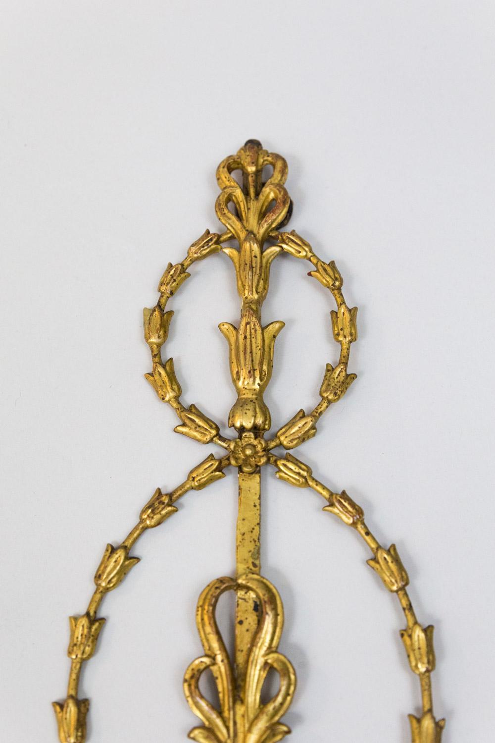 Pair of neoclassical Adam style wall sonces in gilt stucco and metal structure. Model with two-light. Backplate composed of a bottom campanulas chaplet, above the two scrolling arm lights are fixed. Beneath, campanulas swags interlaced issuing in