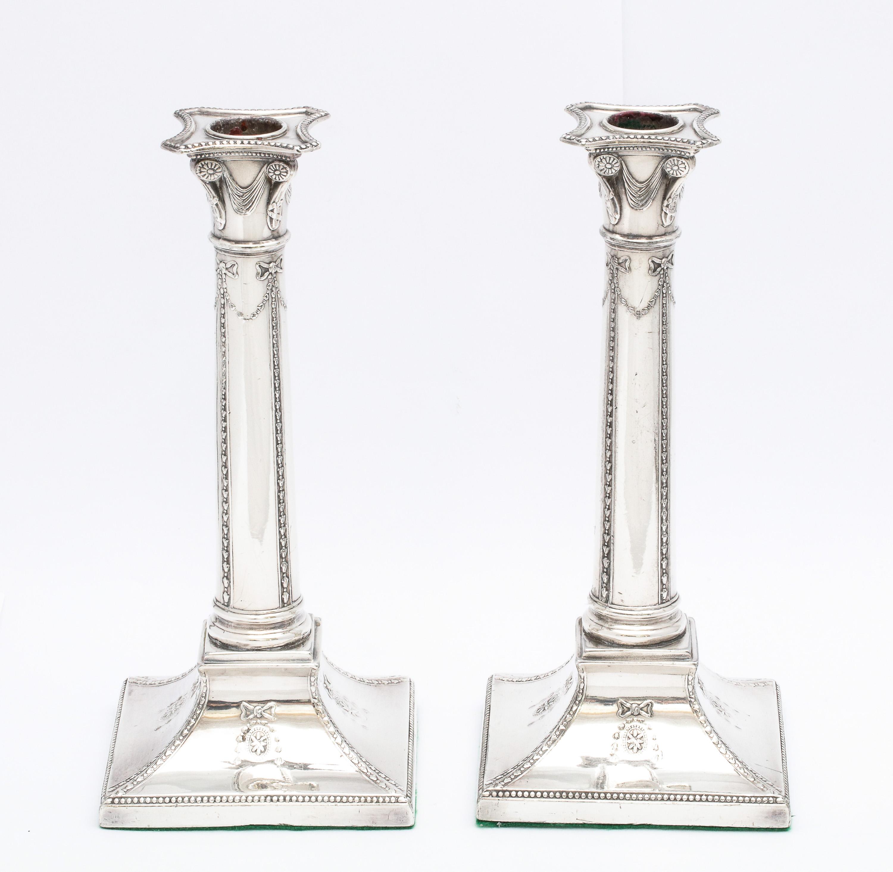 Pair of Adams-style, Sheffield plated, column-form candlesticks, England, circa 1900. Each candlestick measures over 9 1/4 inches high x 4 inches wide (across base) x 4 inches deep (across base). Weighted. Underside is covered in green felt. Plating