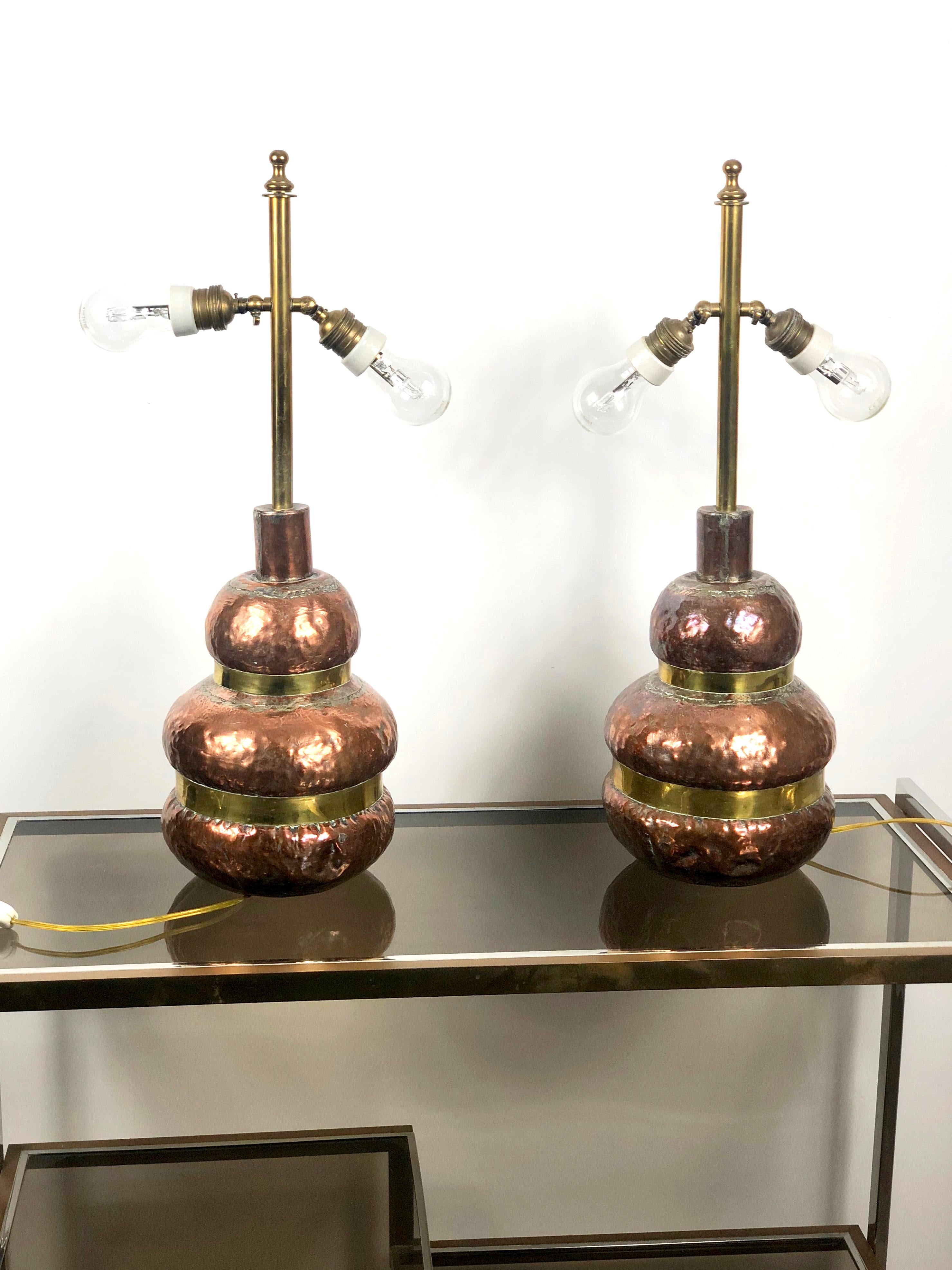 These two table lamps are made in copper and present a circular shape with a brass stick from which depart two adjustable light bulbs. They are sold without the lampshade, but the customer can put on them any lampshade he/she likes. Made in